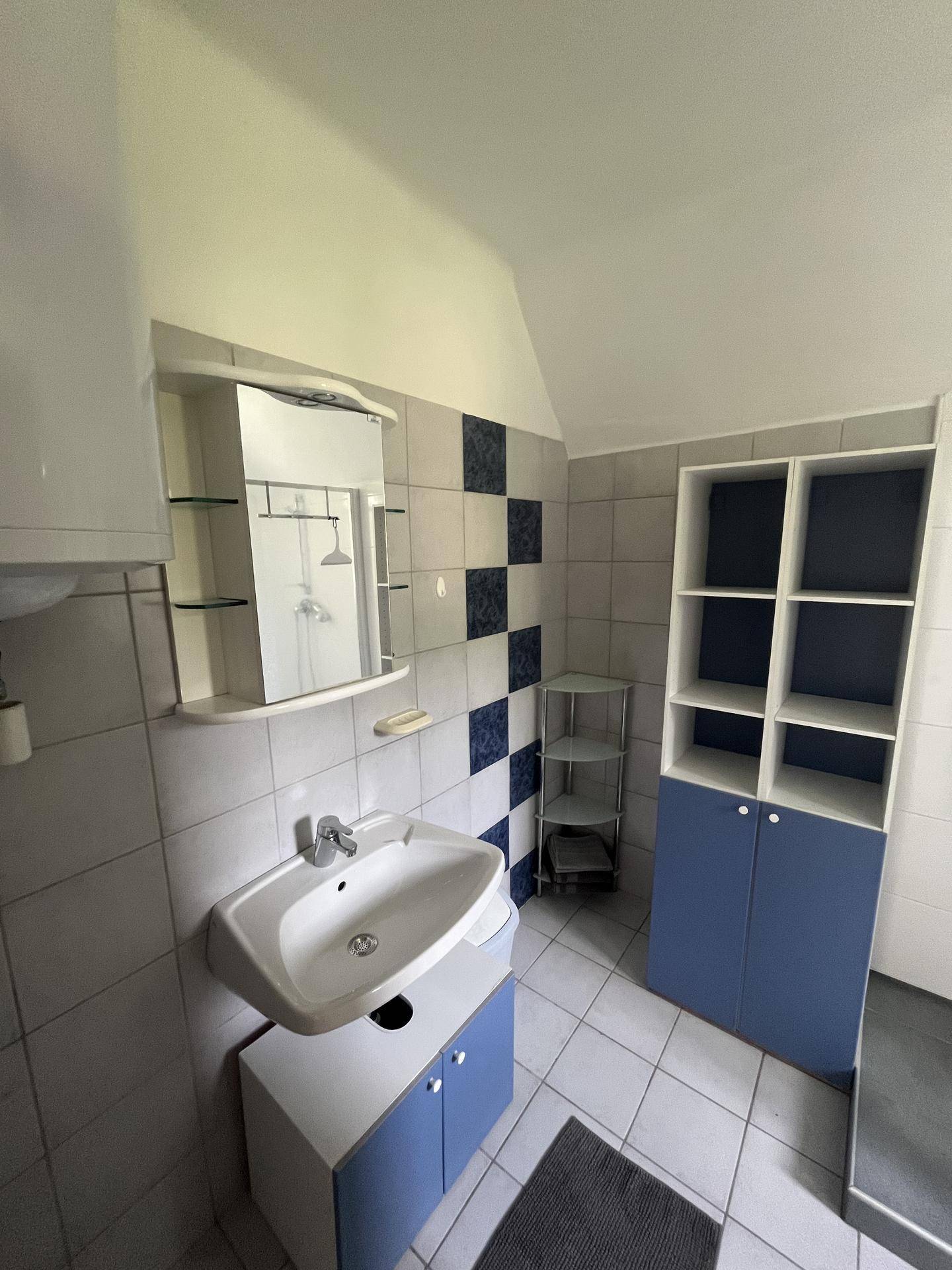 Helles Badezimmer mit Waschbecken, Spiegelschrank und blauen Akzentfliesen an der Wand.