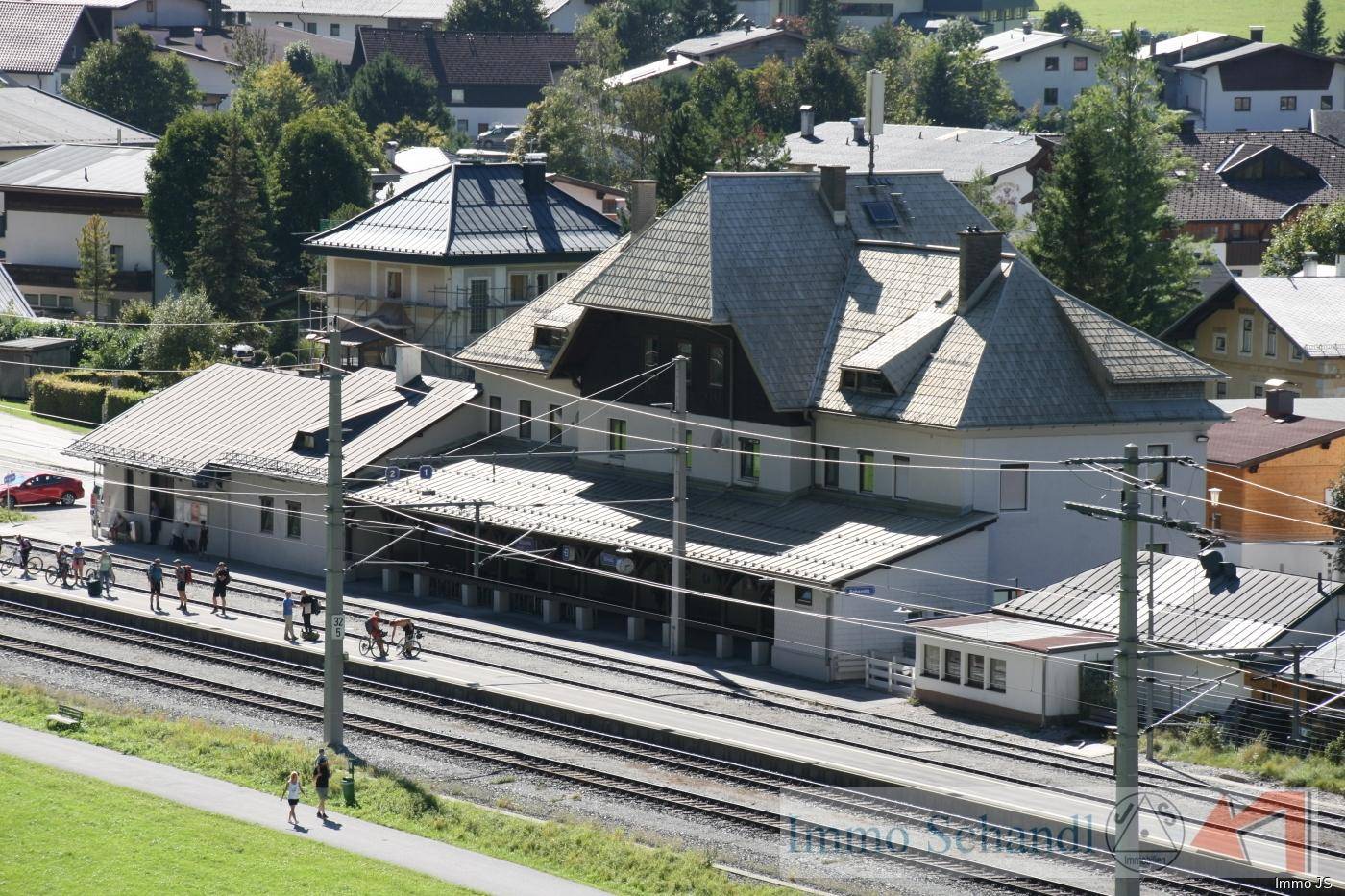 Eine erhöhte Nahaufnahme eines Bahnhofsgebäudes mit Bahnsteigen, Gleisen und umliegenden Häusern.