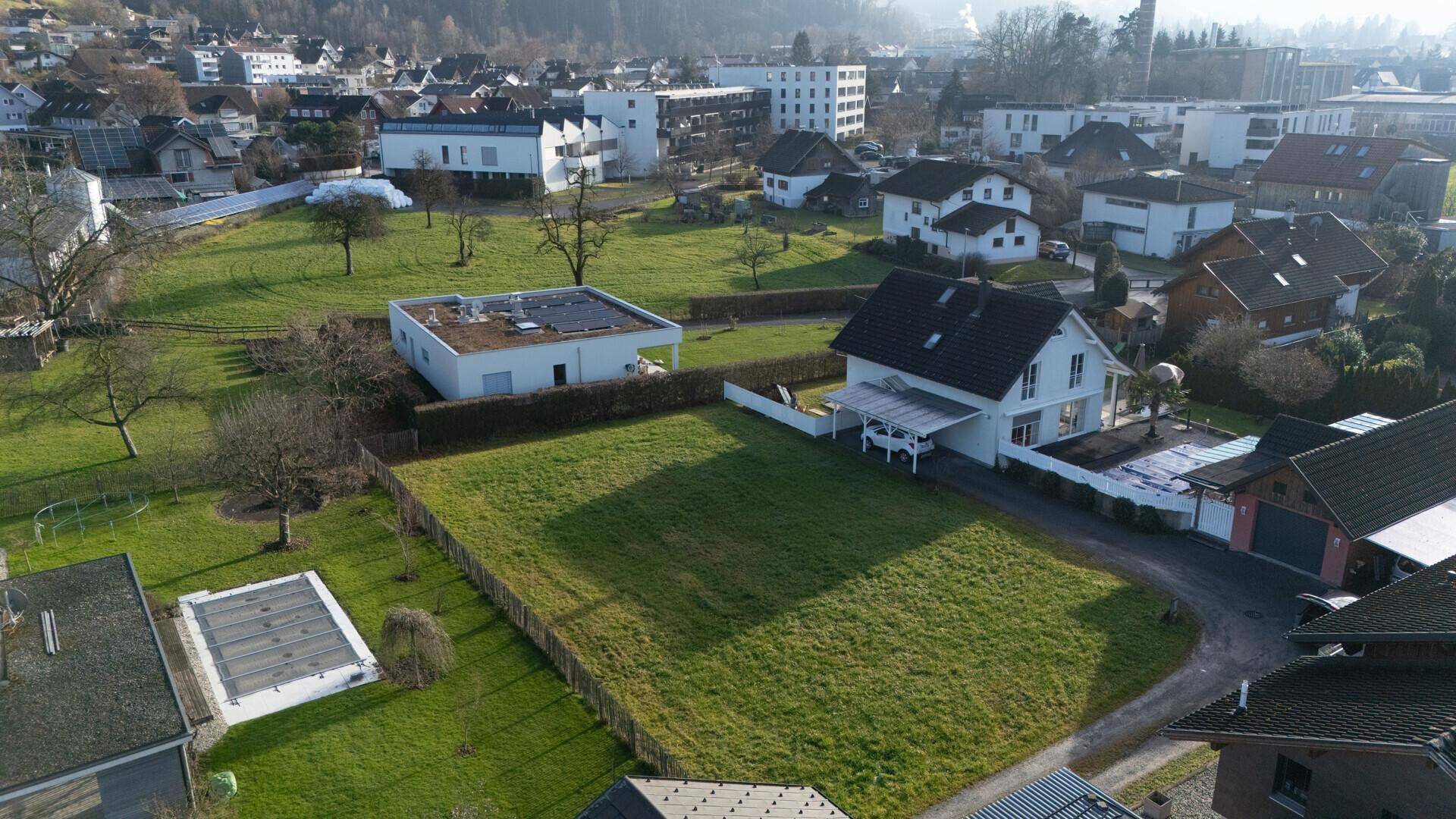 Luftaufnahme eines sonnigen Grundstücks mit umliegenden Häusern und einem Pool in der Nachbarschaft.