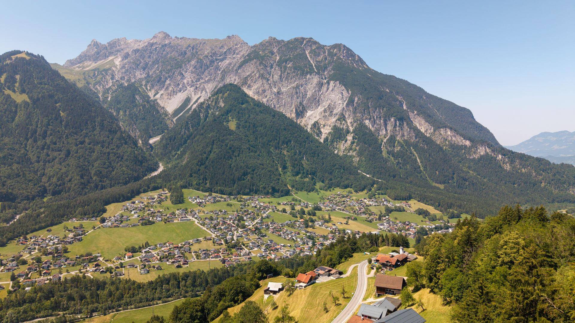 Beeindruckende Luftaufnahme eines Dorfes vor einer Kulisse imposanter Berge und weitreichender Täler.