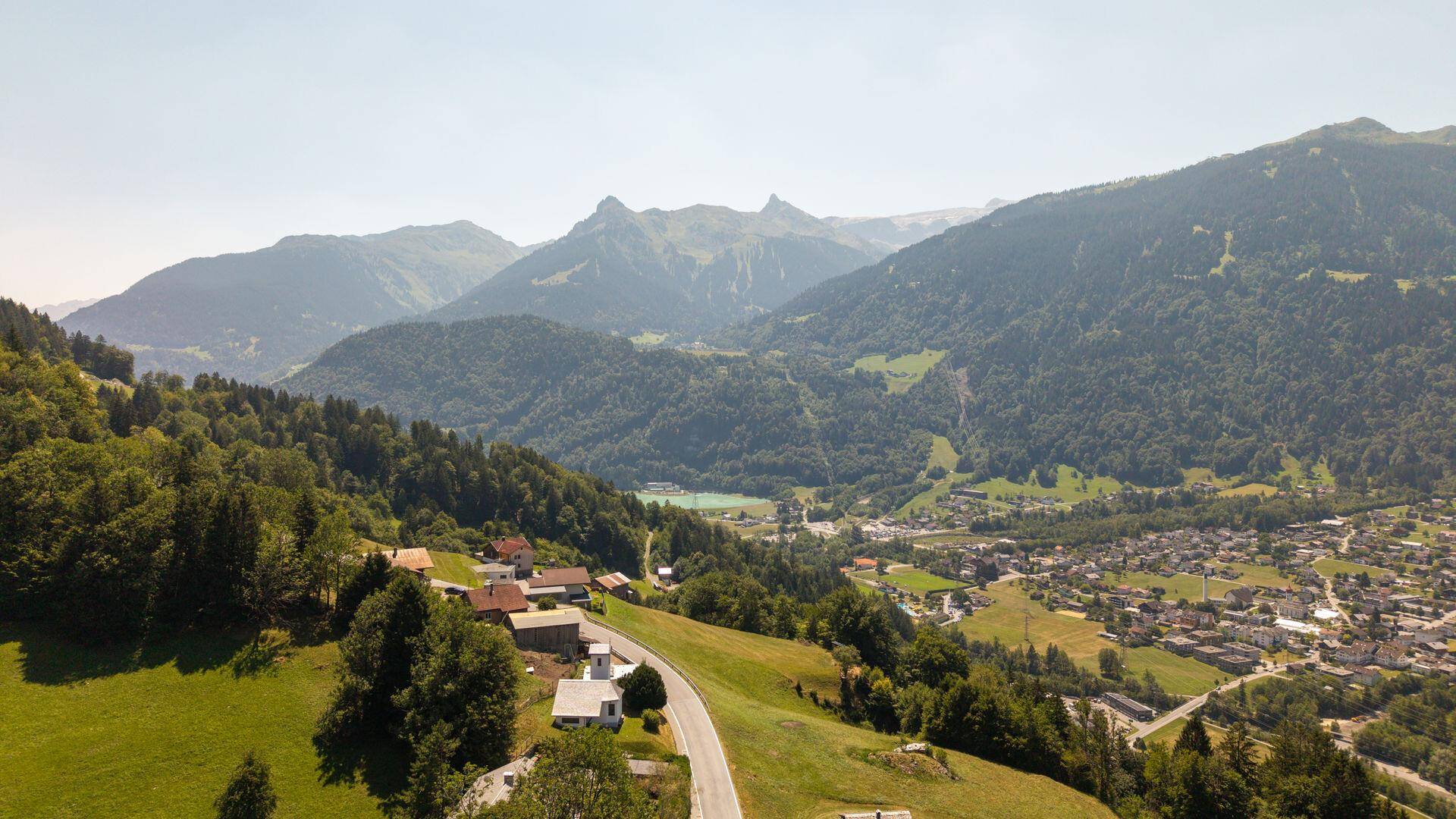 Weitläufige Luftaufnahme eines Dorfes mit Blick auf einen See und die umliegende Berglandschaft.
