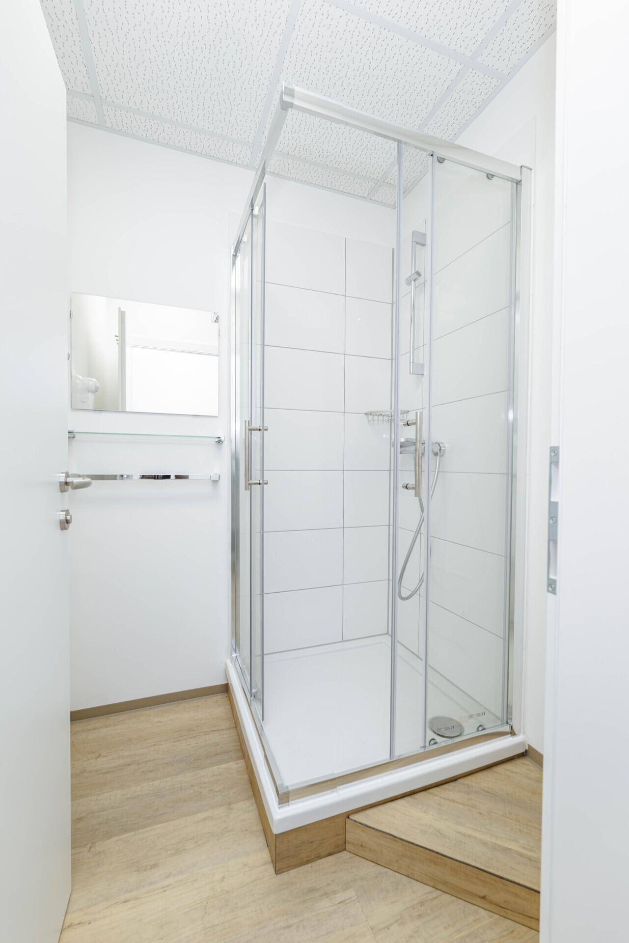 Modernes Badezimmer mit einer Glasduschkabine, weißen Fliesen und hellem Boden.