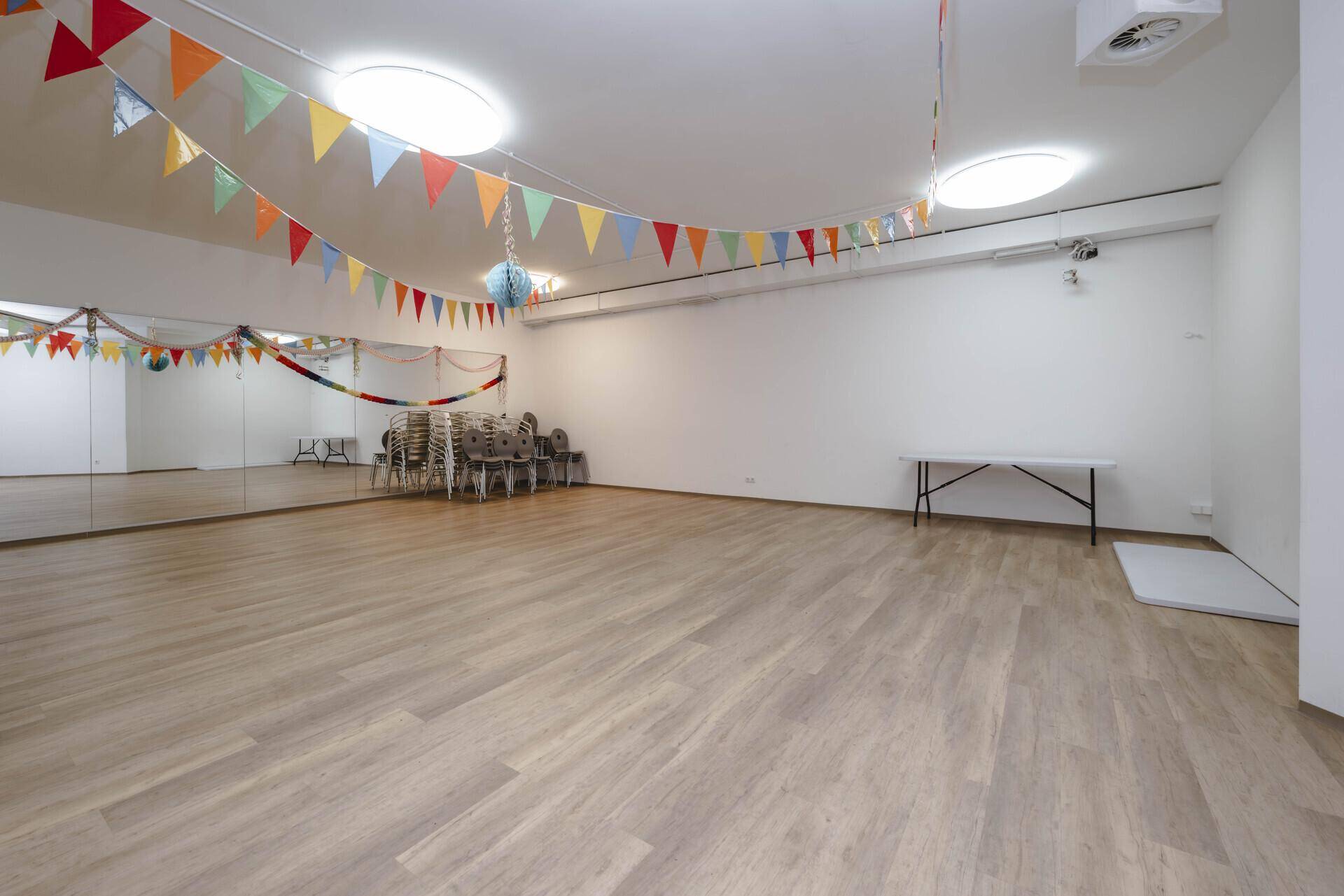 Großer Veranstaltungsraum mit Spiegelwand, hellem Laminatboden und bunten Partygirlanden.