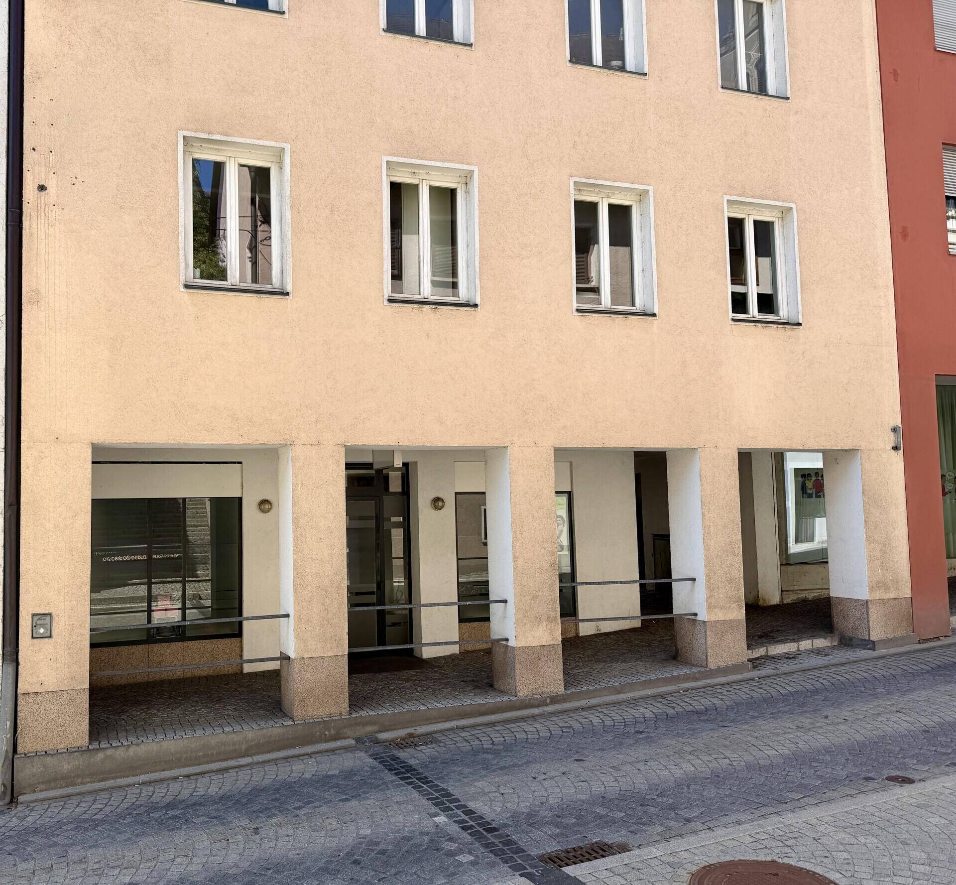 Fassade eines mehrstöckigen Gebäudes mit hellbeiger Farbe und mehreren Fenstern über einem Arkadengang.