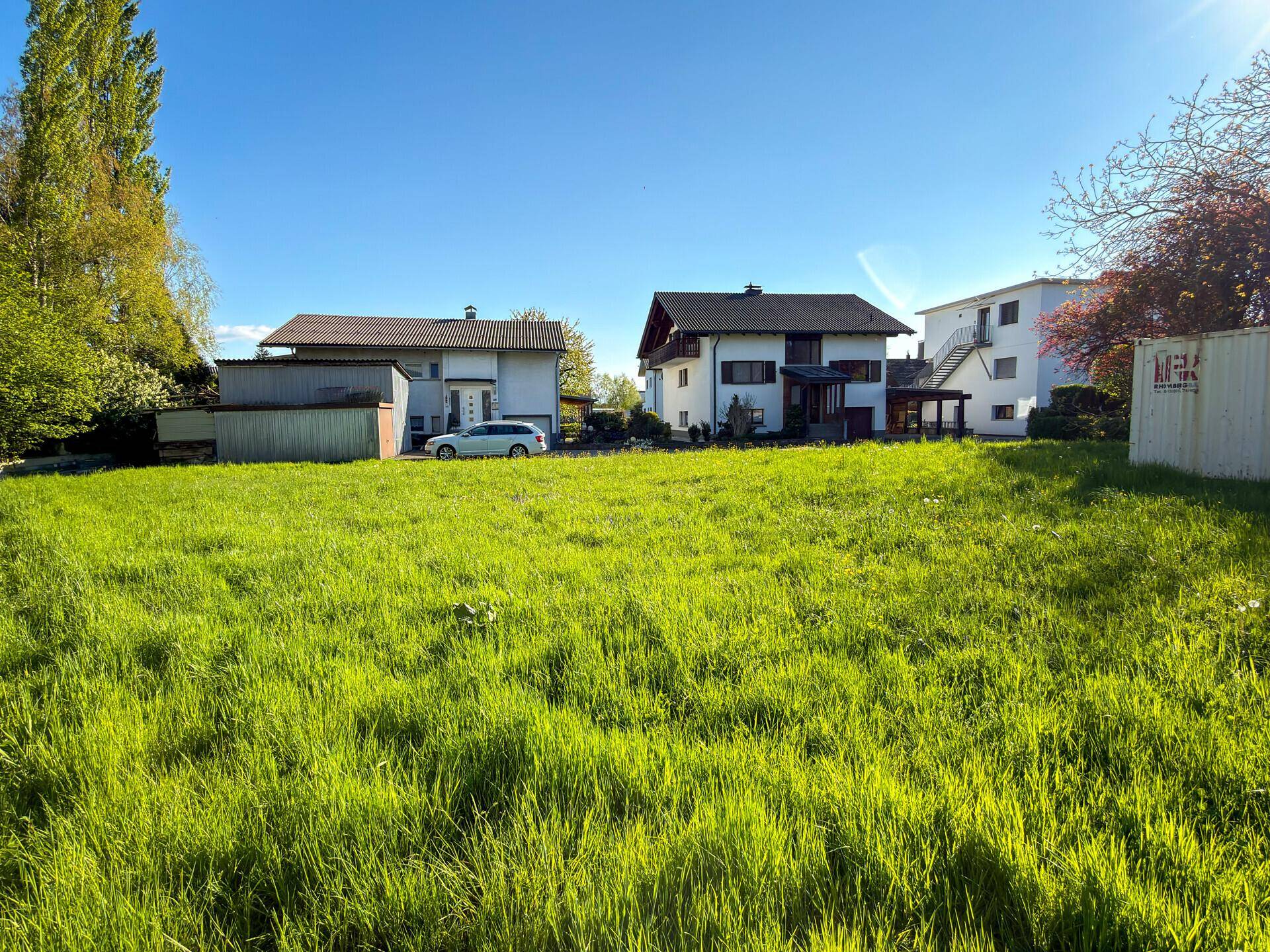 Weitläufige Grünfläche mit Blick auf benachbarte Wohnhäuser unter strahlend blauem Himmel.