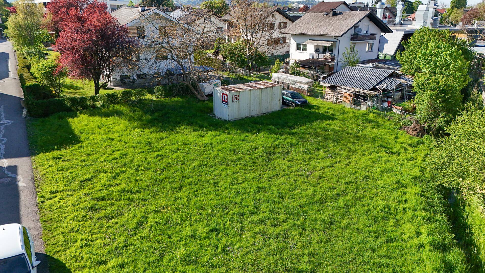 Übersicht aus der Luft über ein großes, sonniges Grundstück mit umliegenden Häusern und einer Straße.