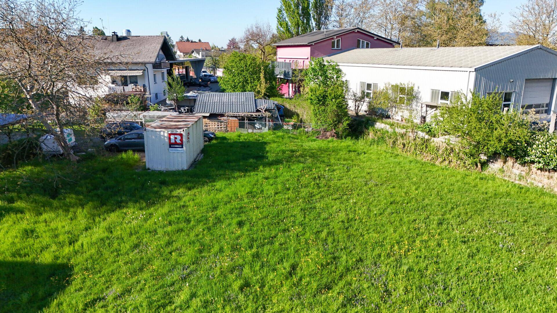 Vogelperspektive auf ein weitläufiges grünes Grundstück mit angrenzenden Gebäuden und Bäumen.