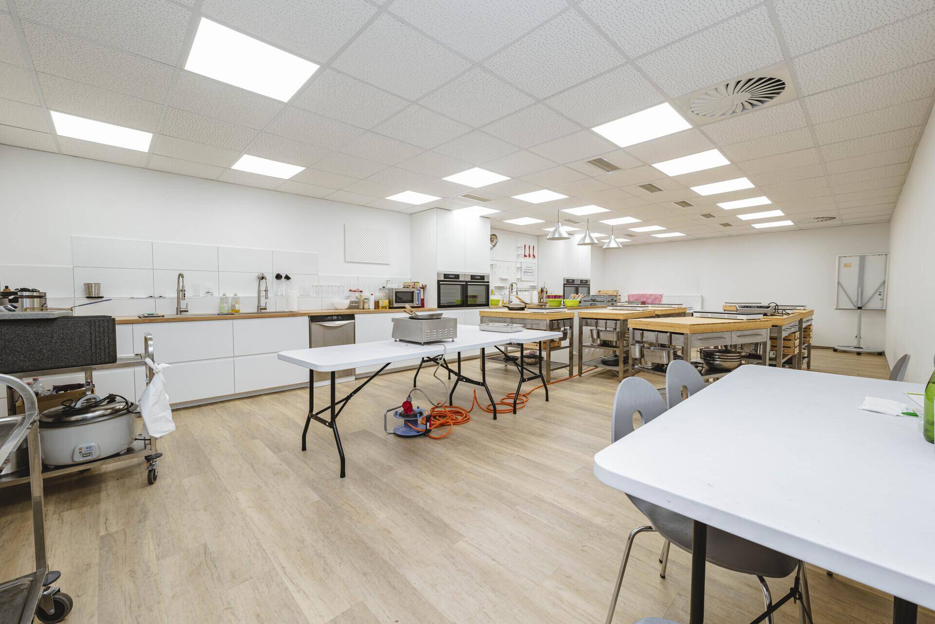 Professionelle Eventküche mit mehreren Arbeitsstationen, weißen Schränken und modernen Geräten.