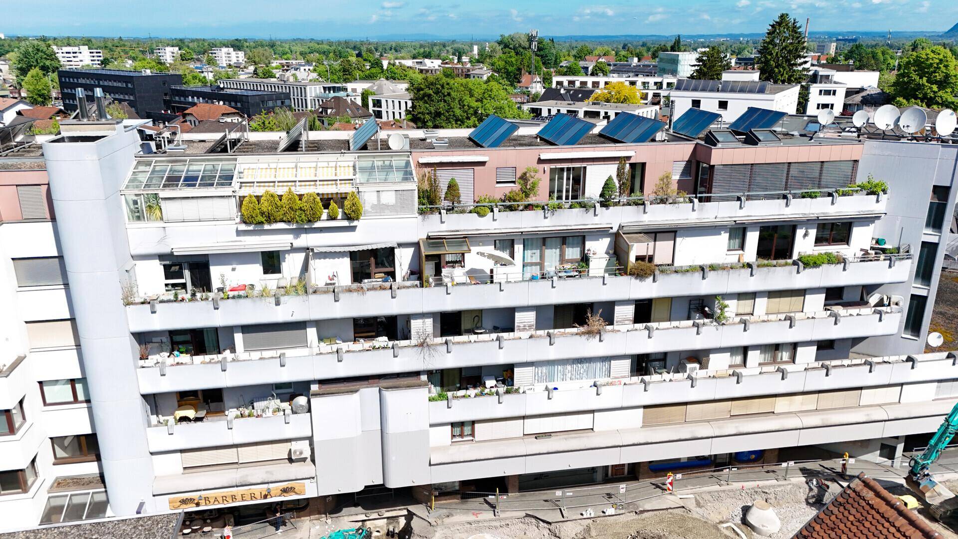 Luftaufnahme eines Mehrfamilienhauses mit Balkonen, Terrassen und Solaranlagen auf dem Dach.