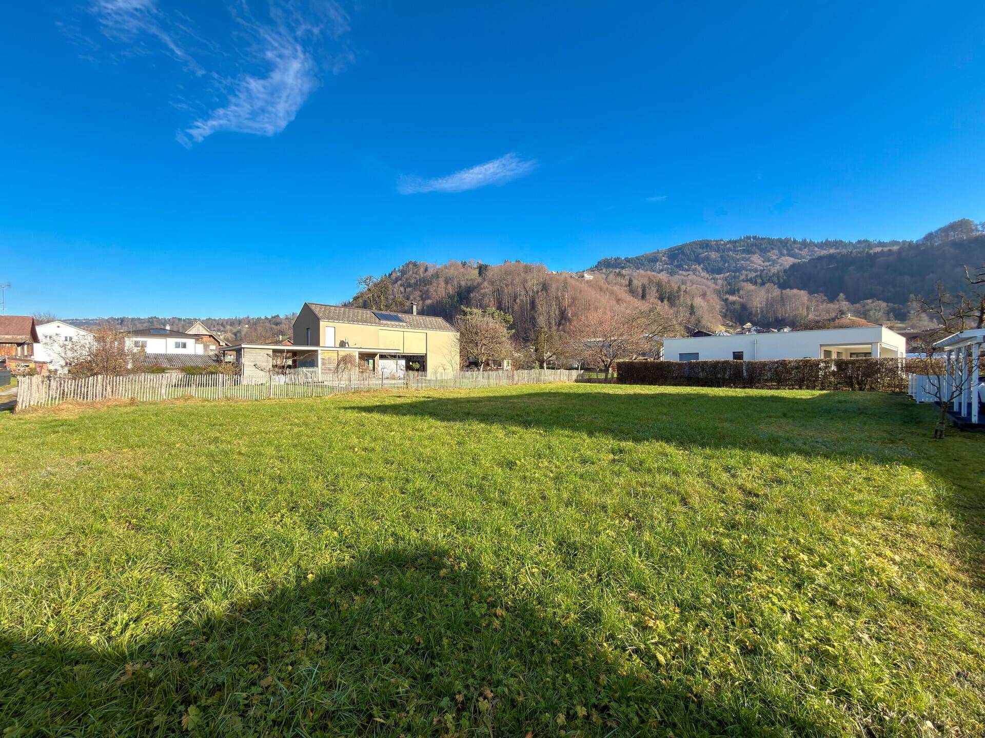 Weitläufige grüne Wiese mit Blick auf die bewaldeten Hügel und benachbarte Wohnhäuser.