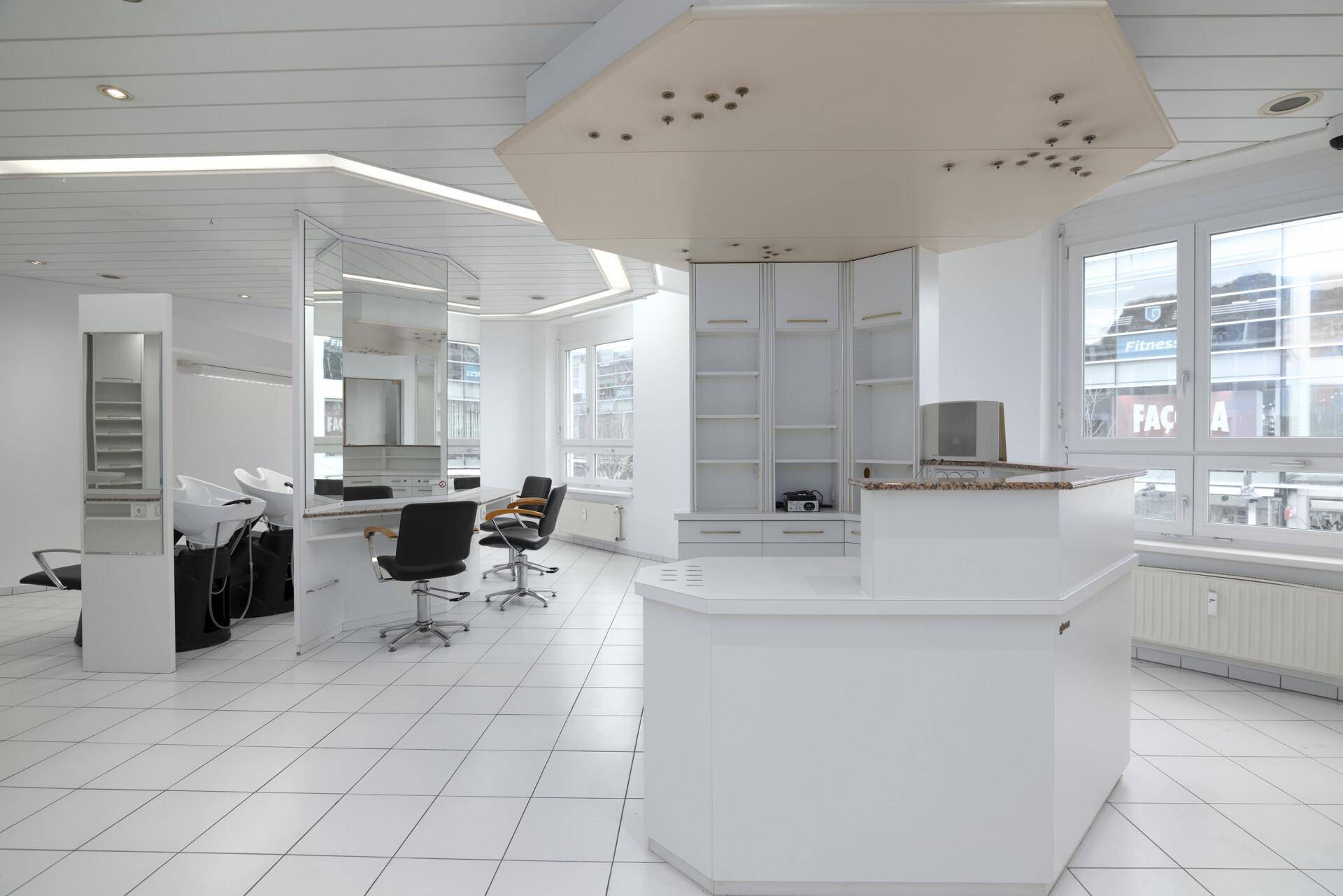 Innenansicht eines Friseursalons mit mehreren Arbeitsplätzen, Waschbecken und großzügigen Fenstern.