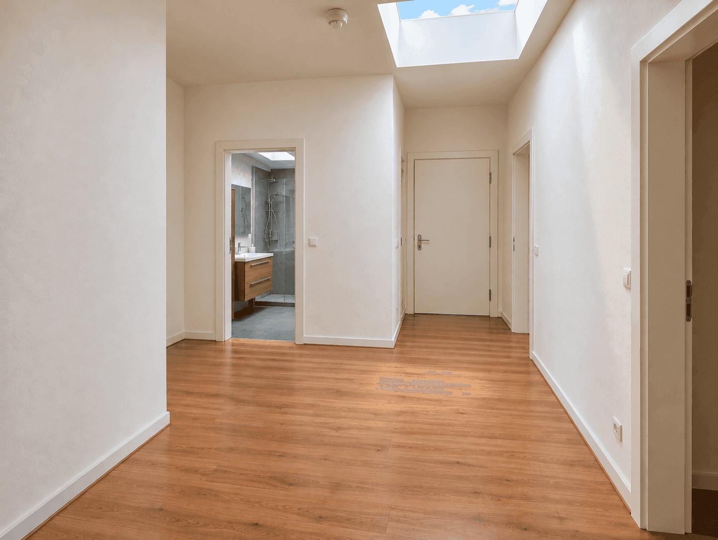 Gangbereich mit Holzboden, Oberlicht und Blick in ein modernes Badezimmer.