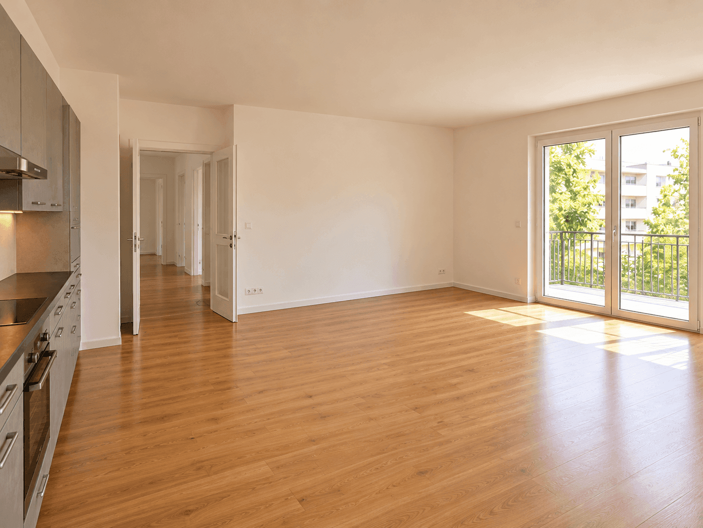 Geräumiges Wohnzimmer mit Holzboden, viel Tageslicht und Zugang zu einem Balkon.