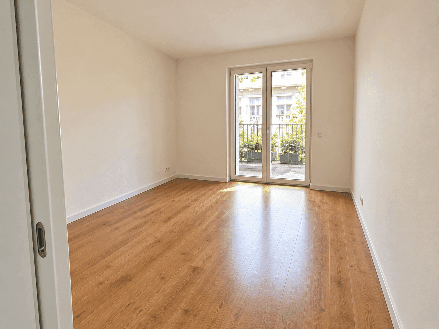 Leeres Schlafzimmer mit Holzboden und direktem Zugang zu einem kleinen Balkon.