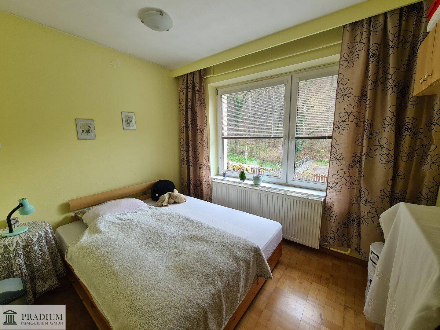 Helles Schlafzimmer mit Doppelbett, Holzboden und Blick in den Garten.