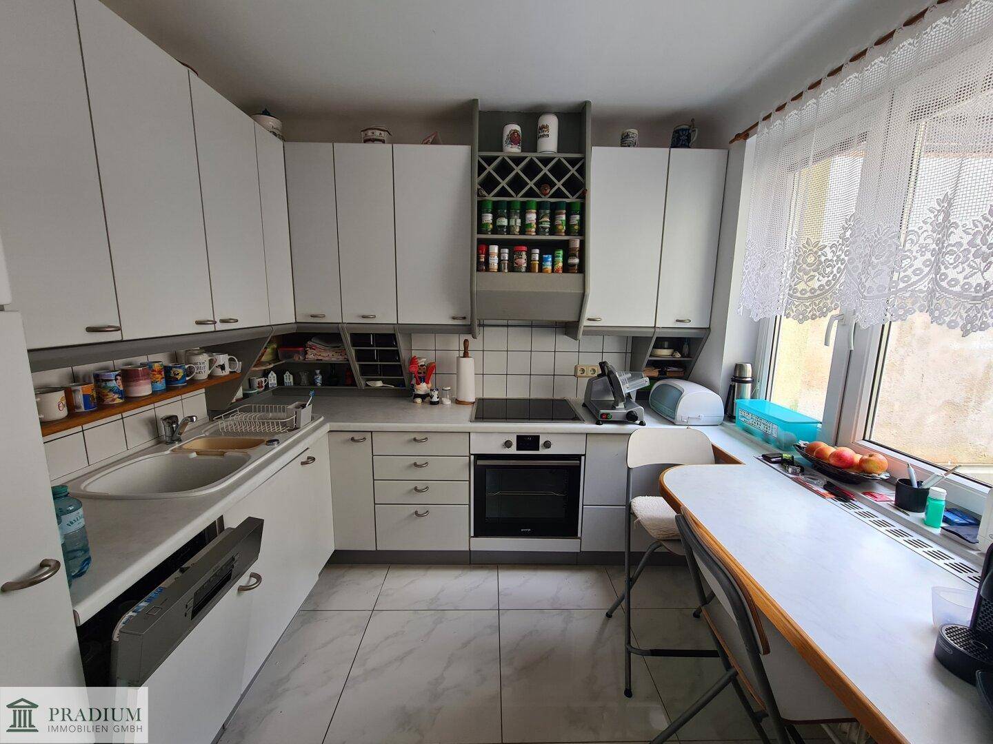 Funktionale Küche mit weißen Schränken, Fliesenboden und Essbereich am Fenster.