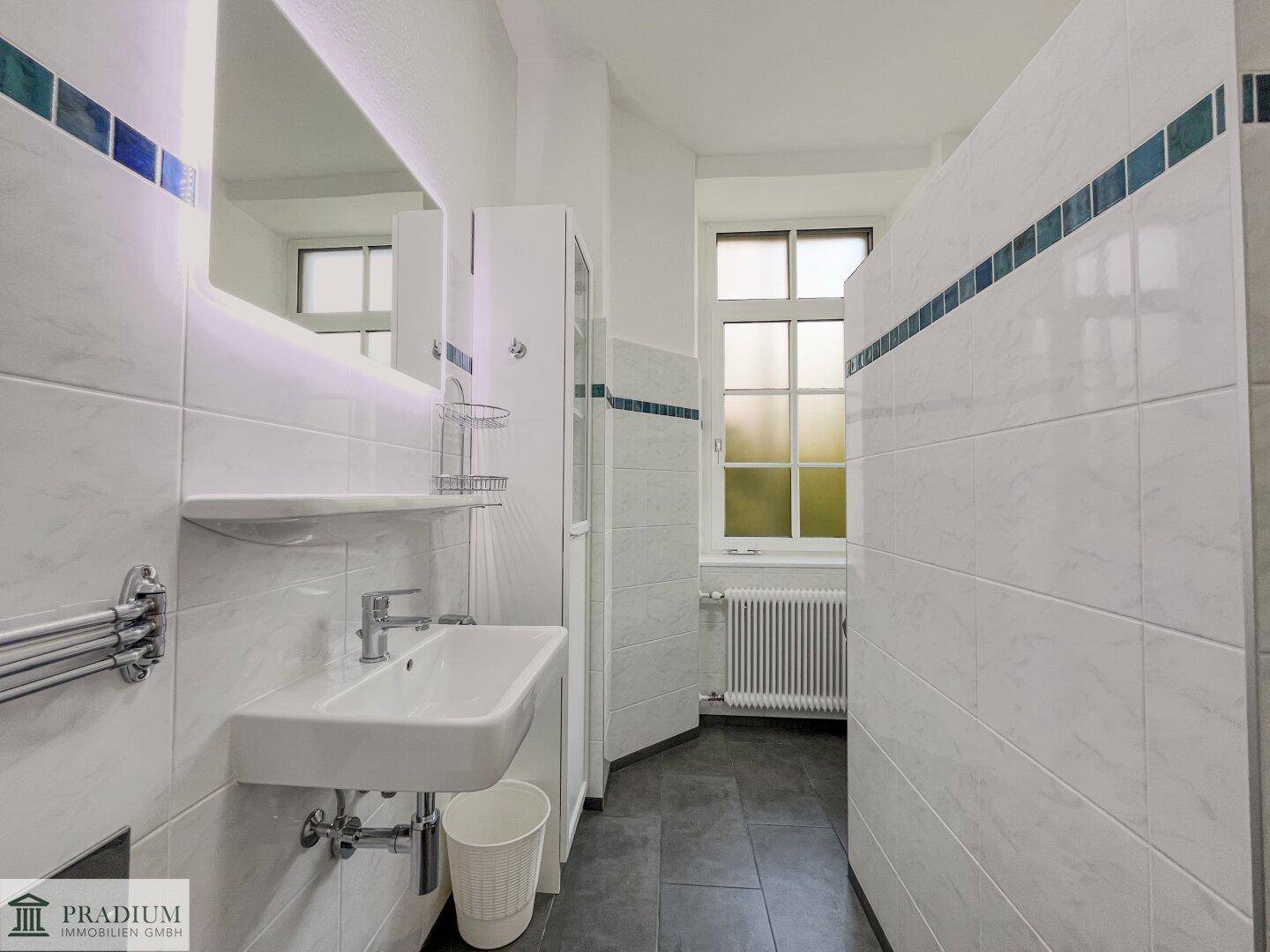 Modernes Badezimmer mit Waschbecken, beleuchtetem Spiegel und Fenster für natürliche Belüftung.