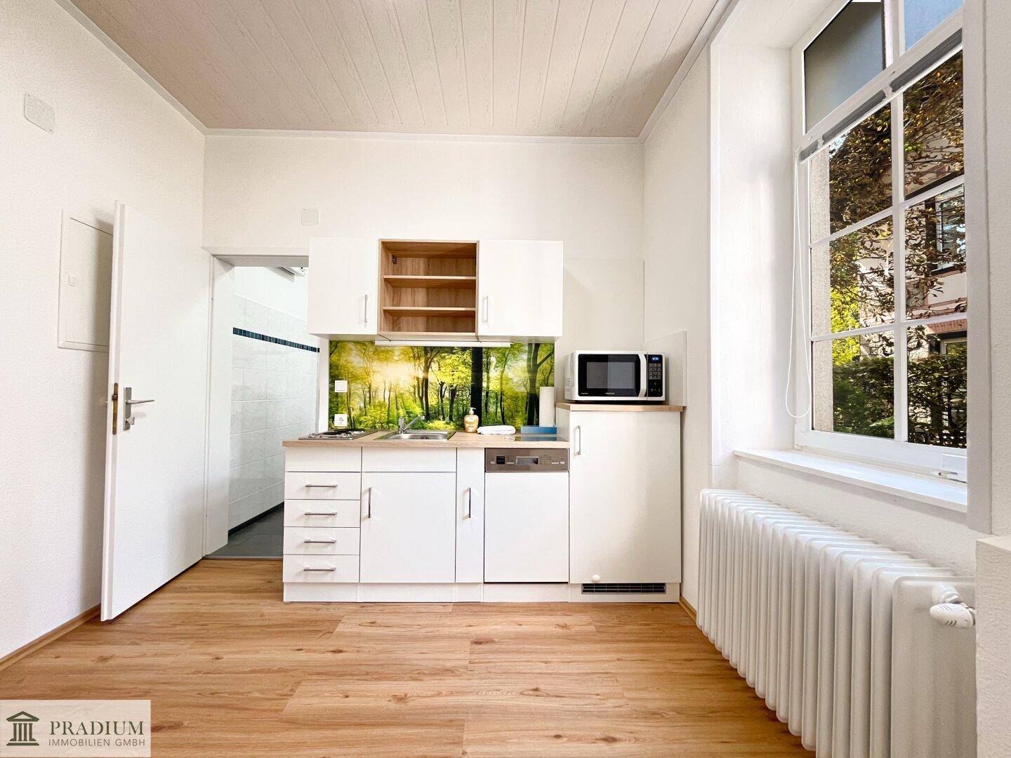 Kleine, moderne Einbauküche mit weißen Schränken, Mikrowelle und Geschirrspüler.