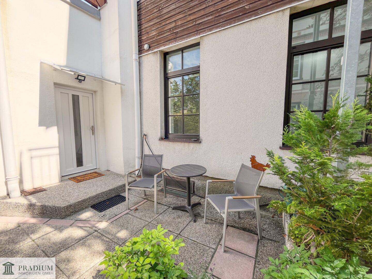 Gemütliche Terrasse mit Sitzgelegenheiten und Pflanzen vor dem Hauseingang.