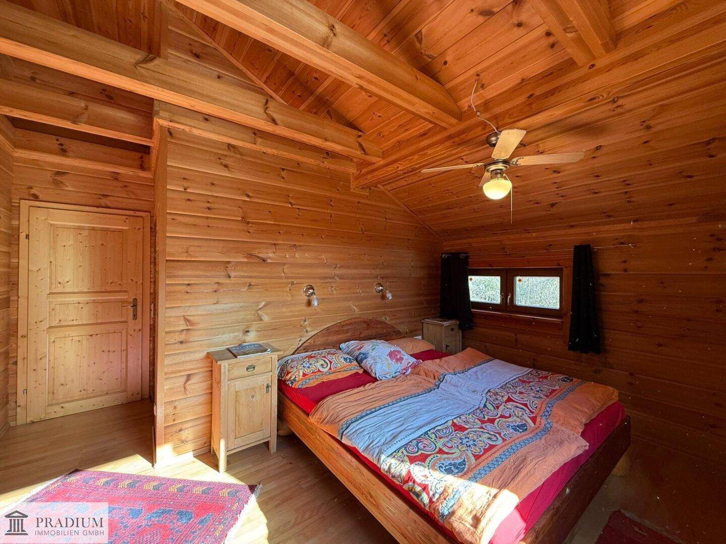 Gemütliches Schlafzimmer mit Holzwänden, Holzbalkendecke und einem Deckenventilator für angenehme Nächte.