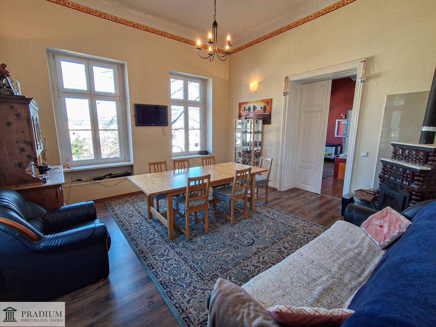 Geräumiger Wohn- und Essbereich mit hohen Decken, Parkettboden und traditionellem Kaminofen.
