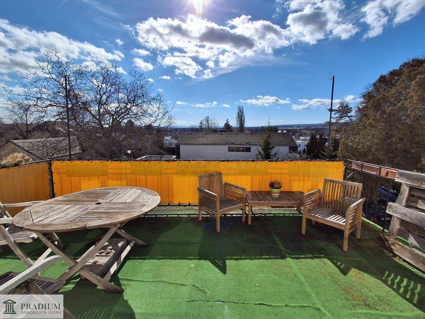 Gemütliche Terrasse mit Holztisch und Stühlen, umgeben von einer gelben Sichtschutzwand.