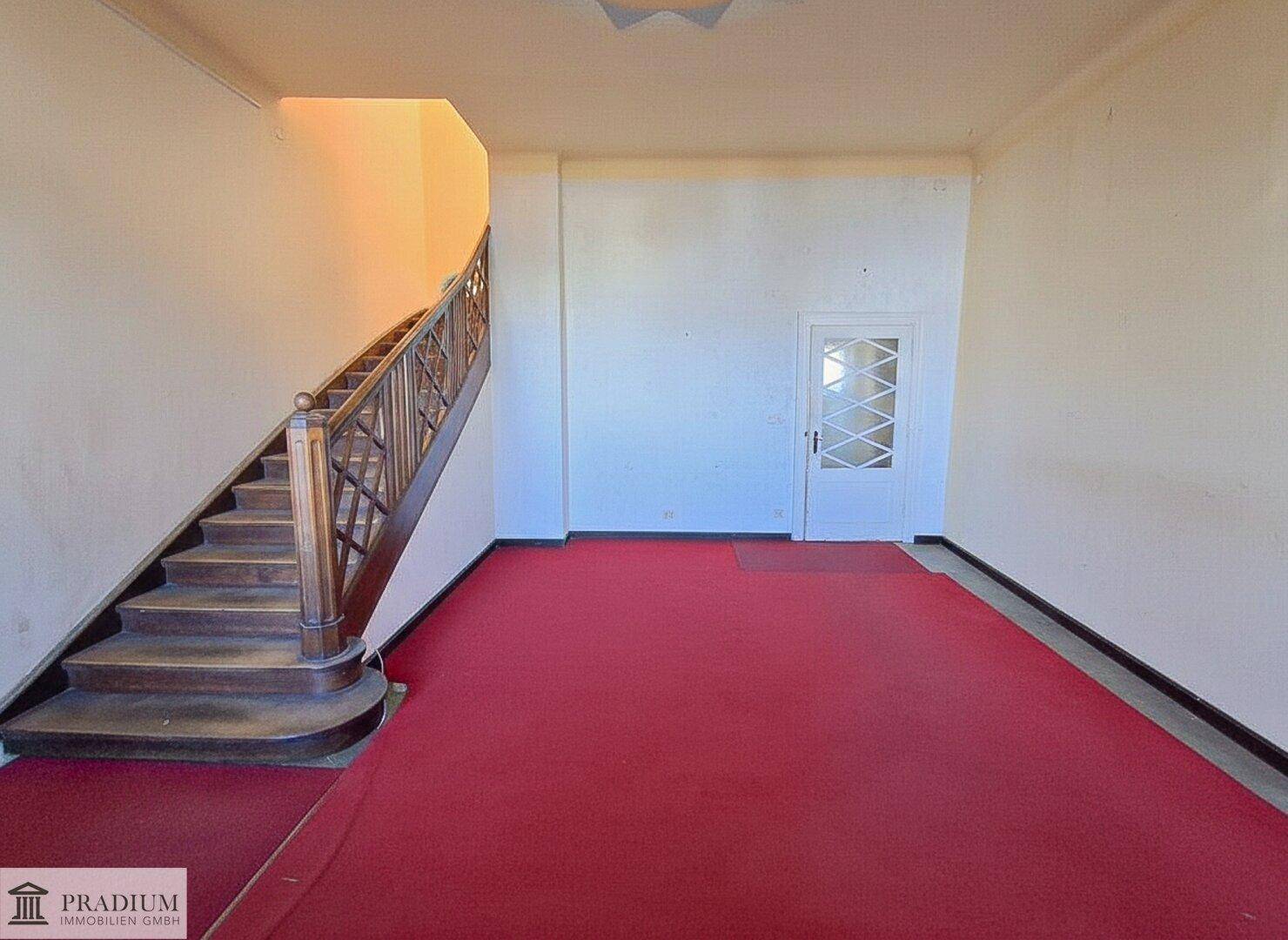 Geräumiger Flur mit breiter Holztreppe und rotem Teppichboden.