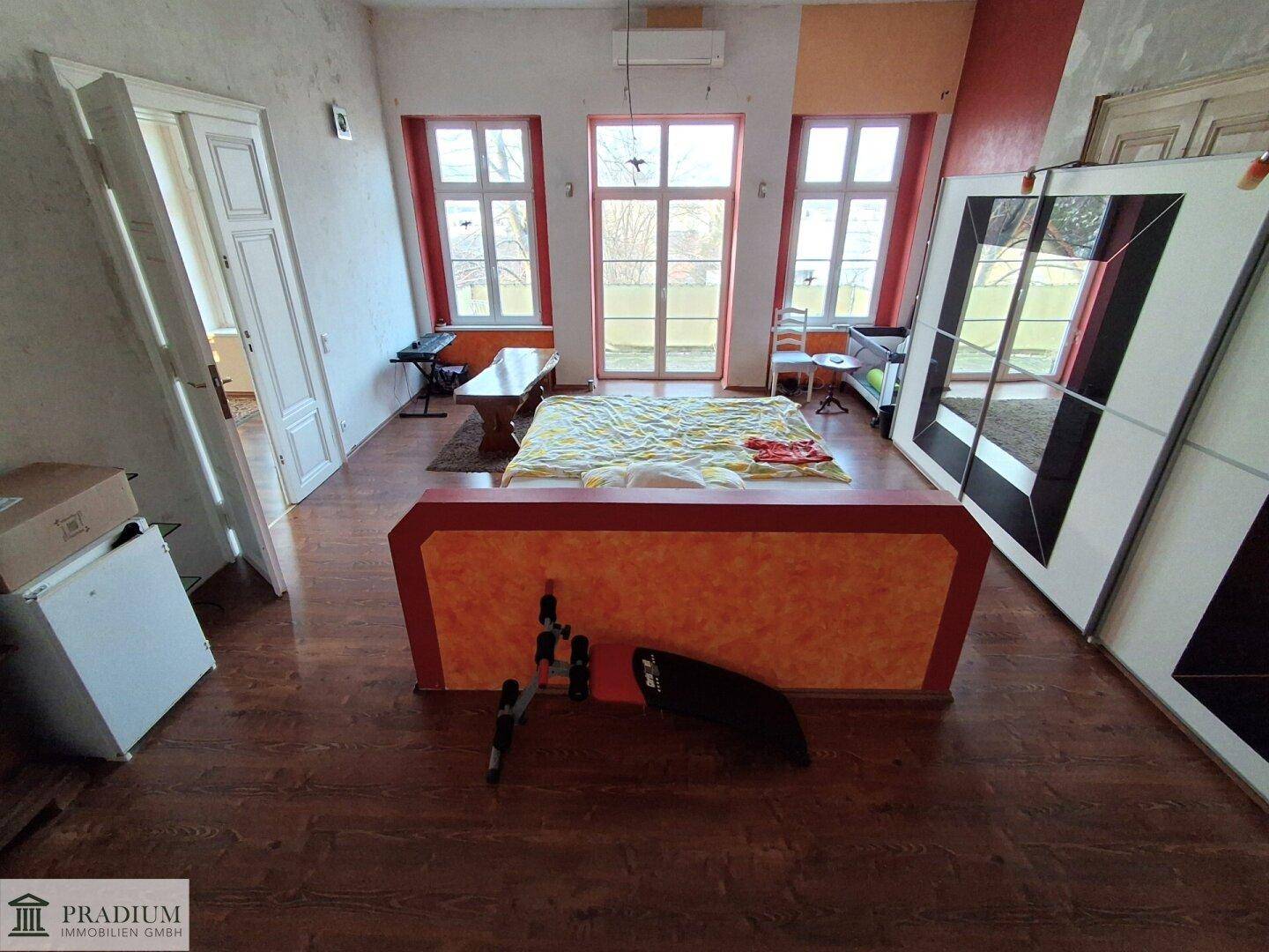 Helles Schlafzimmer mit Holzboden, großen Fenstern und Zugang zu einem Außenbereich.