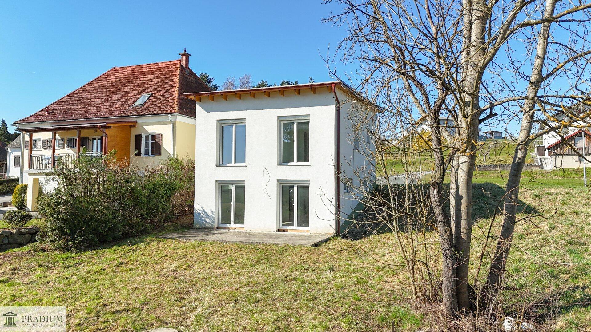 Neubau-Einfamilienhaus mit weißer Fassade, kleiner Betonfläche und Gartenbereich, bereit zur Gestaltung.