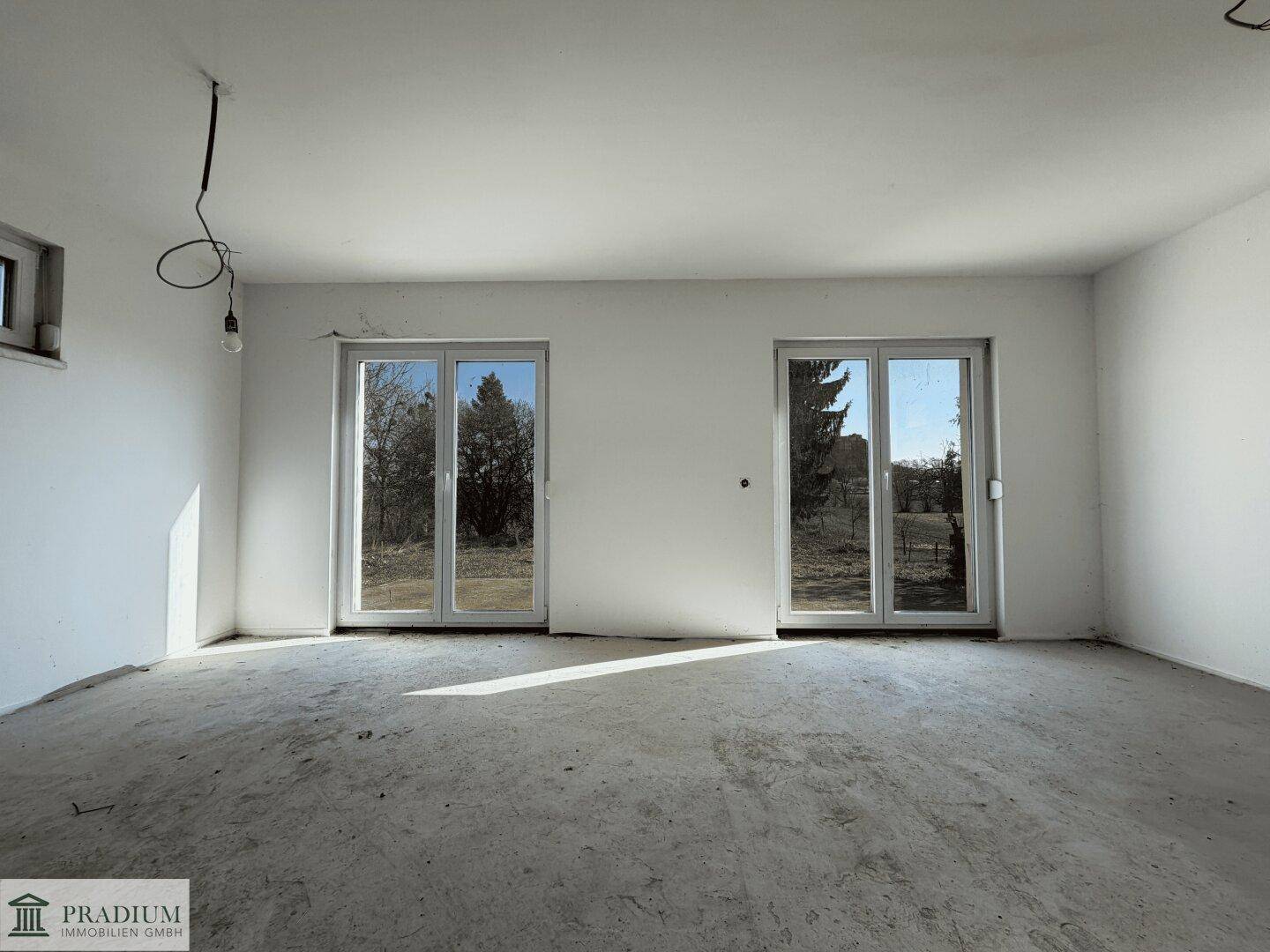 Leerer Wohnbereich mit großen Fenstern und Rohbetonboden, bietet viel Gestaltungspotenzial.