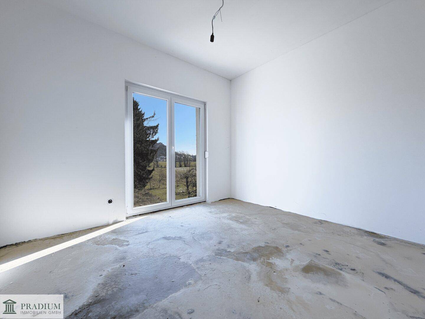 Unmöbliertes Schlafzimmer mit großem Fenster und Rohbetonboden, ideal für individuelle Gestaltung.