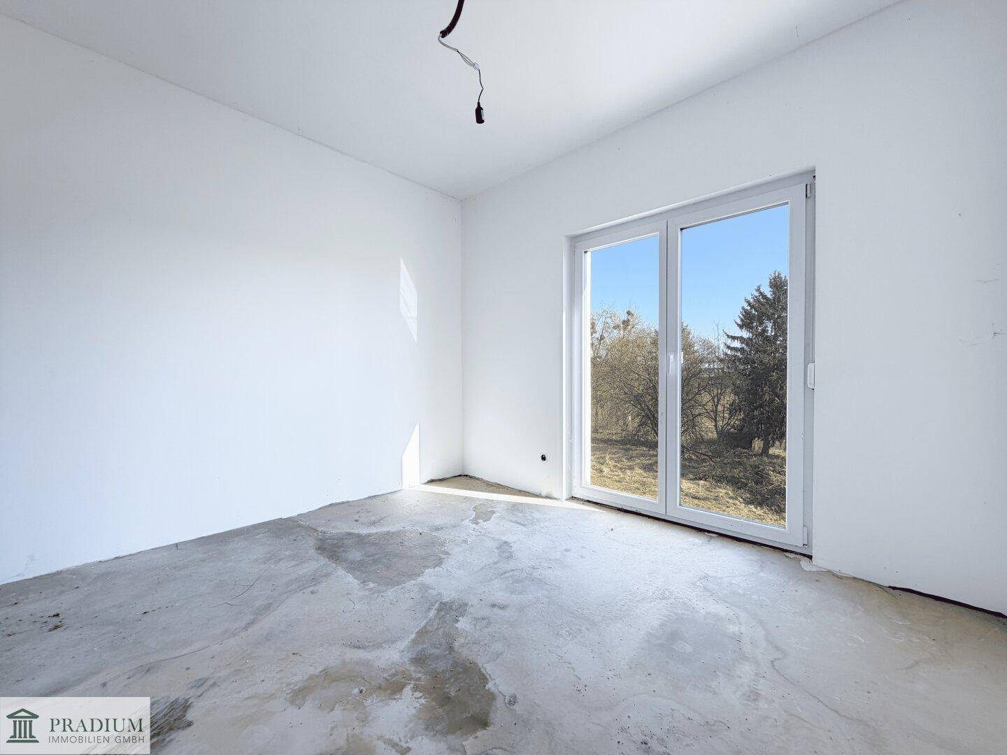 Leeres Schlafzimmer mit großem Fenster und Rohbetonboden, bietet viel Raum für persönliche Einrichtung.