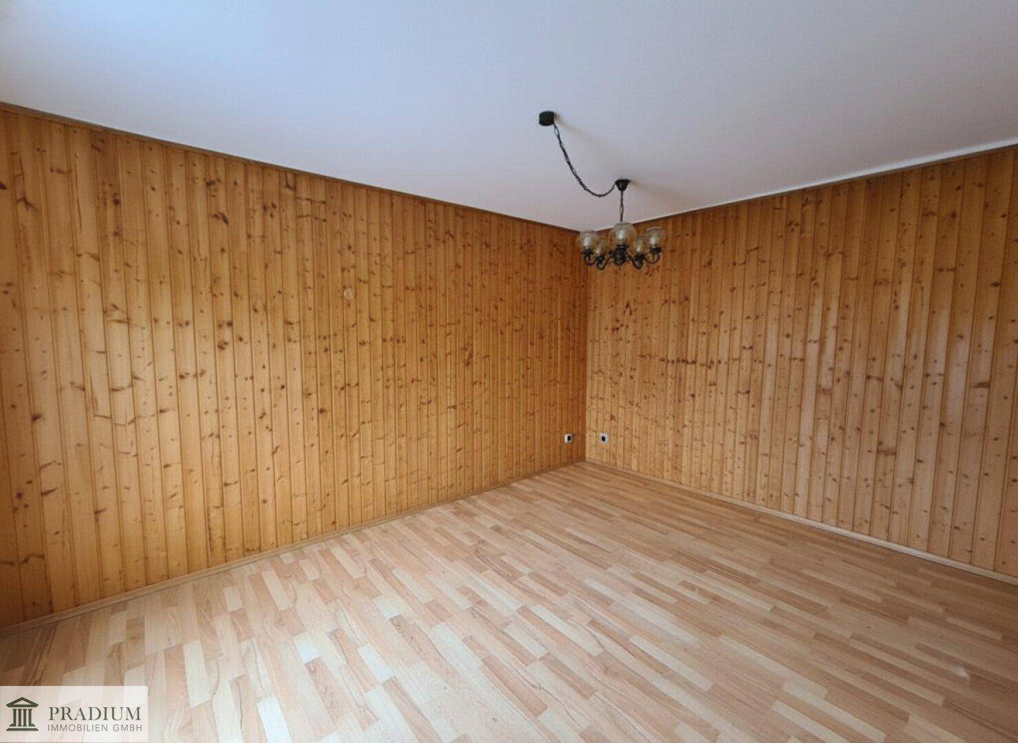 Leerer Raum mit Holzvertäfelung an den Wänden und hellem Laminatboden.