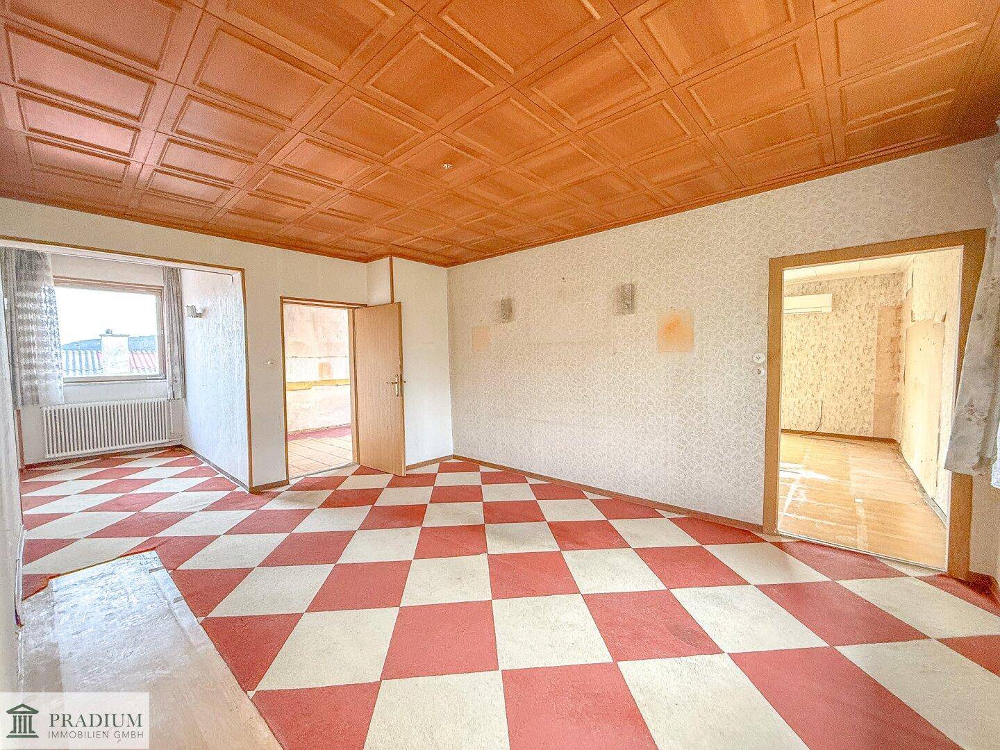 Geräumiger Innenraum mit auffälligem rot-weiß kariertem Boden und holzvertäfelter Decke, bereit zur Renovierung.