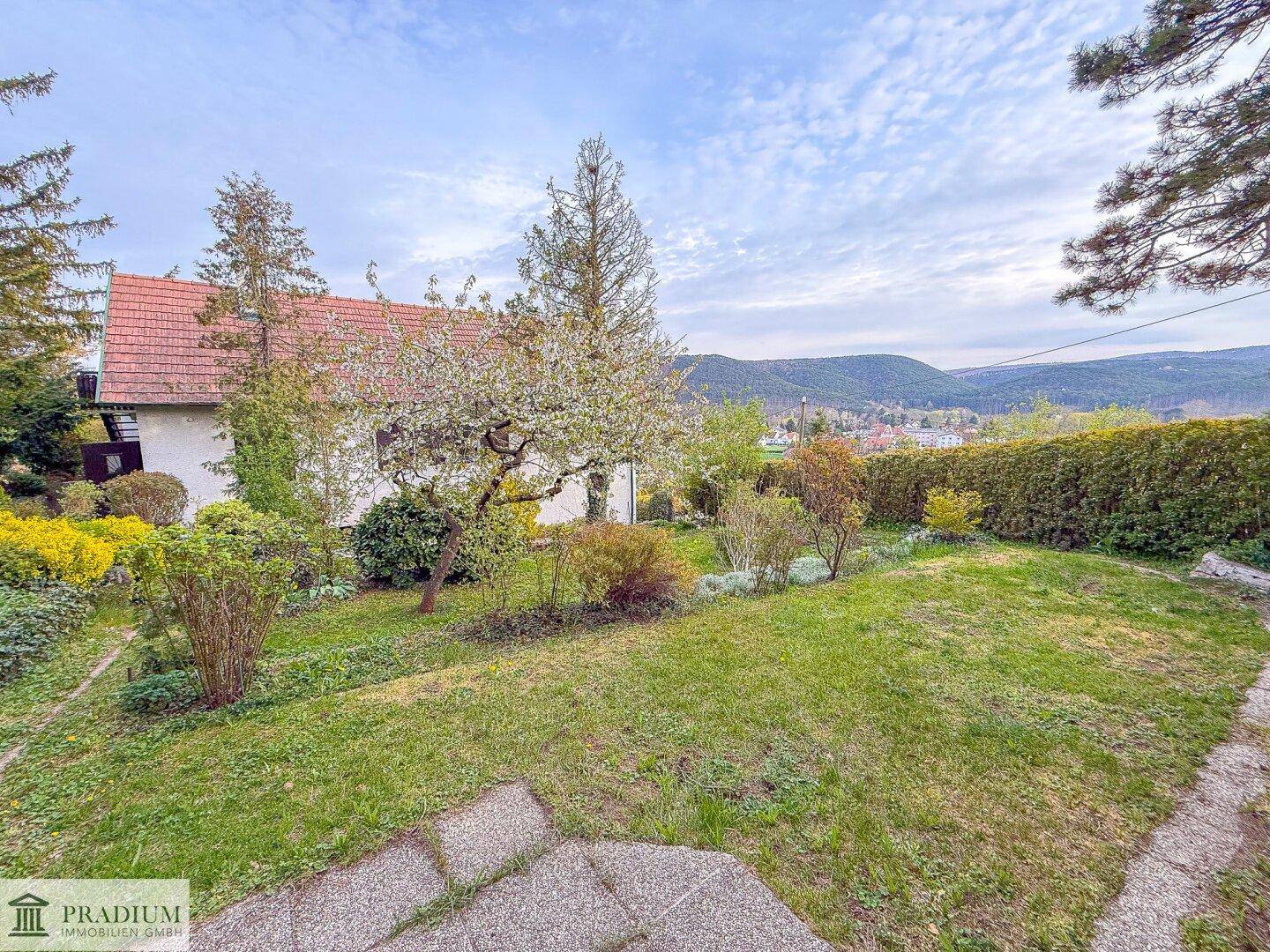Gepflegter Garten mit Rasenfläche, blühenden Bäumen und Blick auf das Haus und die umliegende Landschaft.