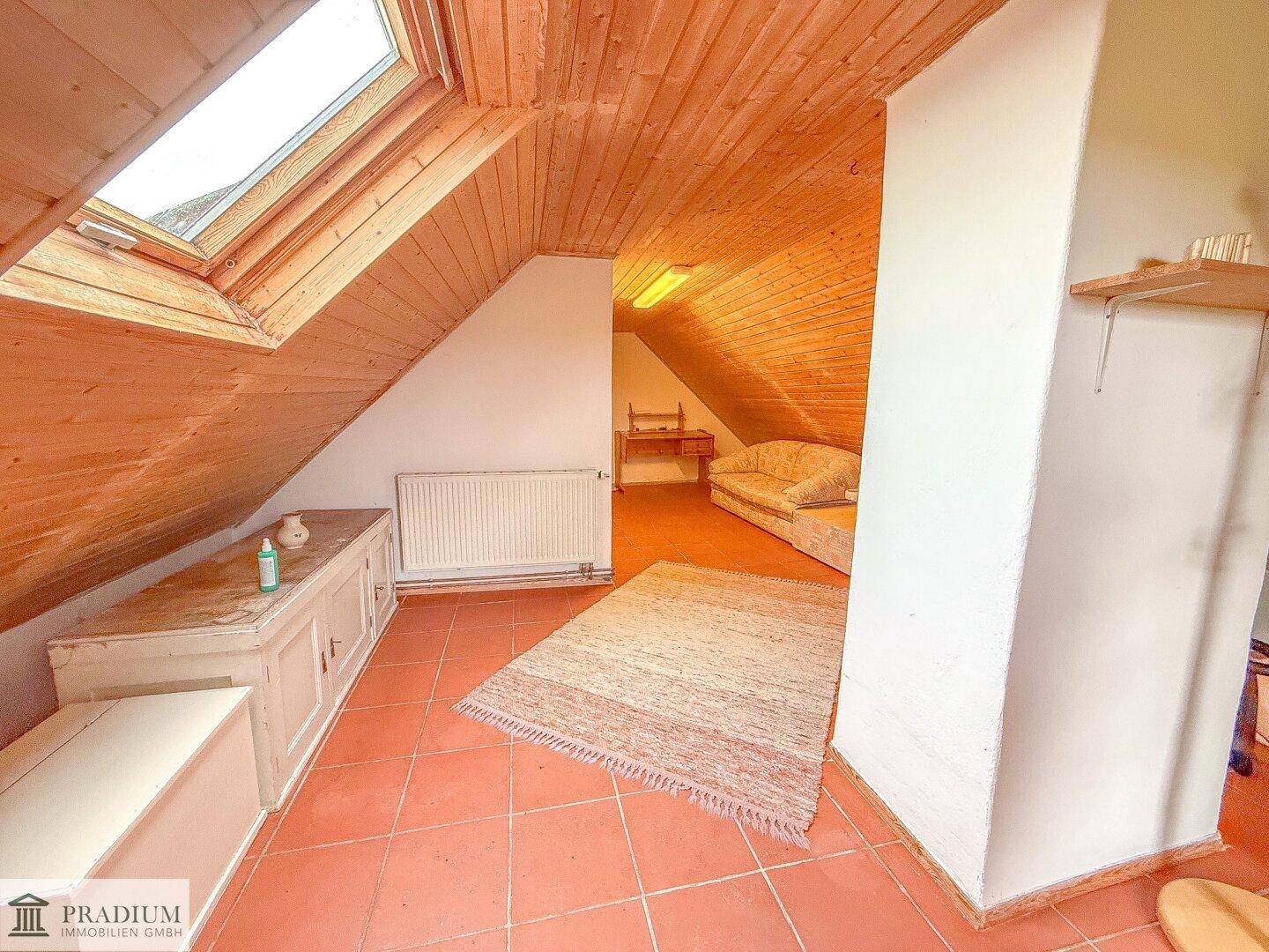 Gemütlicher Dachbodenraum mit holzvertäfelter Schrägdecke, Dachfenster und Terrakotta-Fliesenboden.