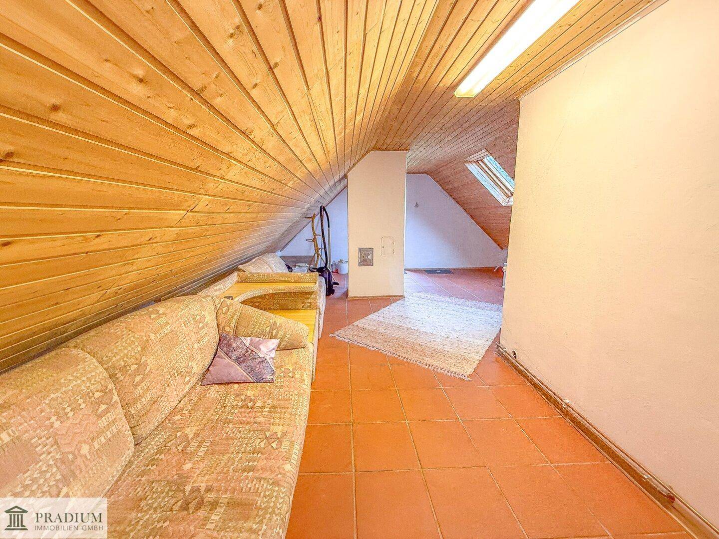 Geräumiger Dachbodenbereich mit holzvertäfelter Schrägdecke und bequemer Couch, ideal als Rückzugsort.