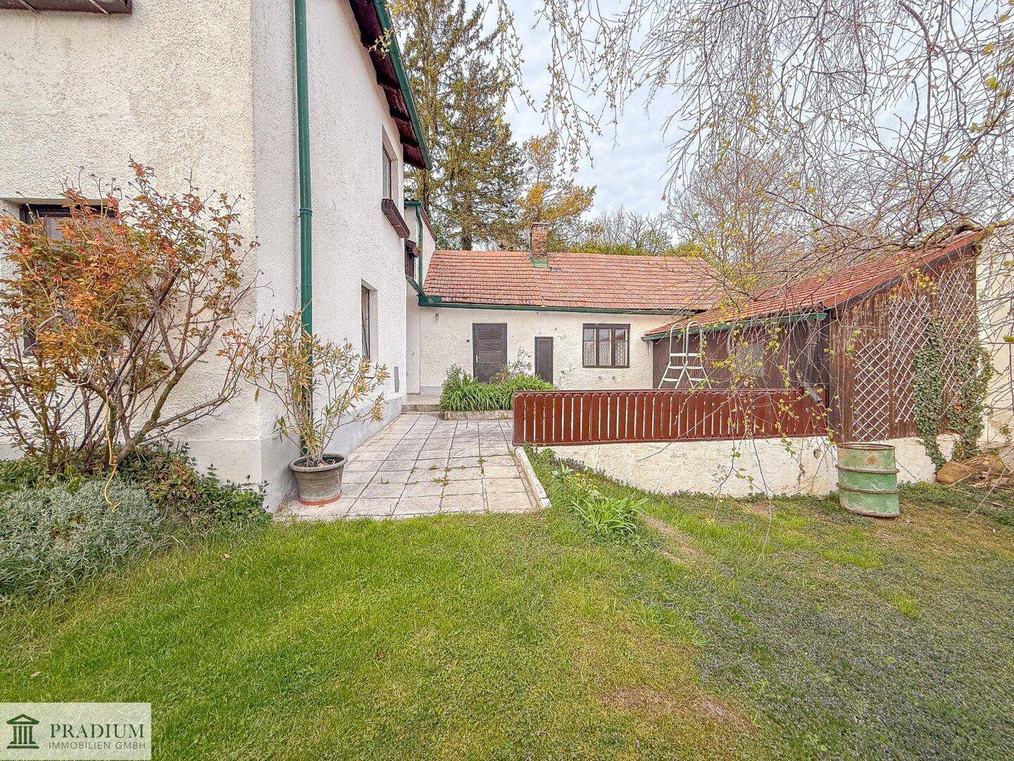 Rückseite des Hauses mit Rasenfläche, gepflastertem Bereich und einem kleinen Schuppen im Garten.
