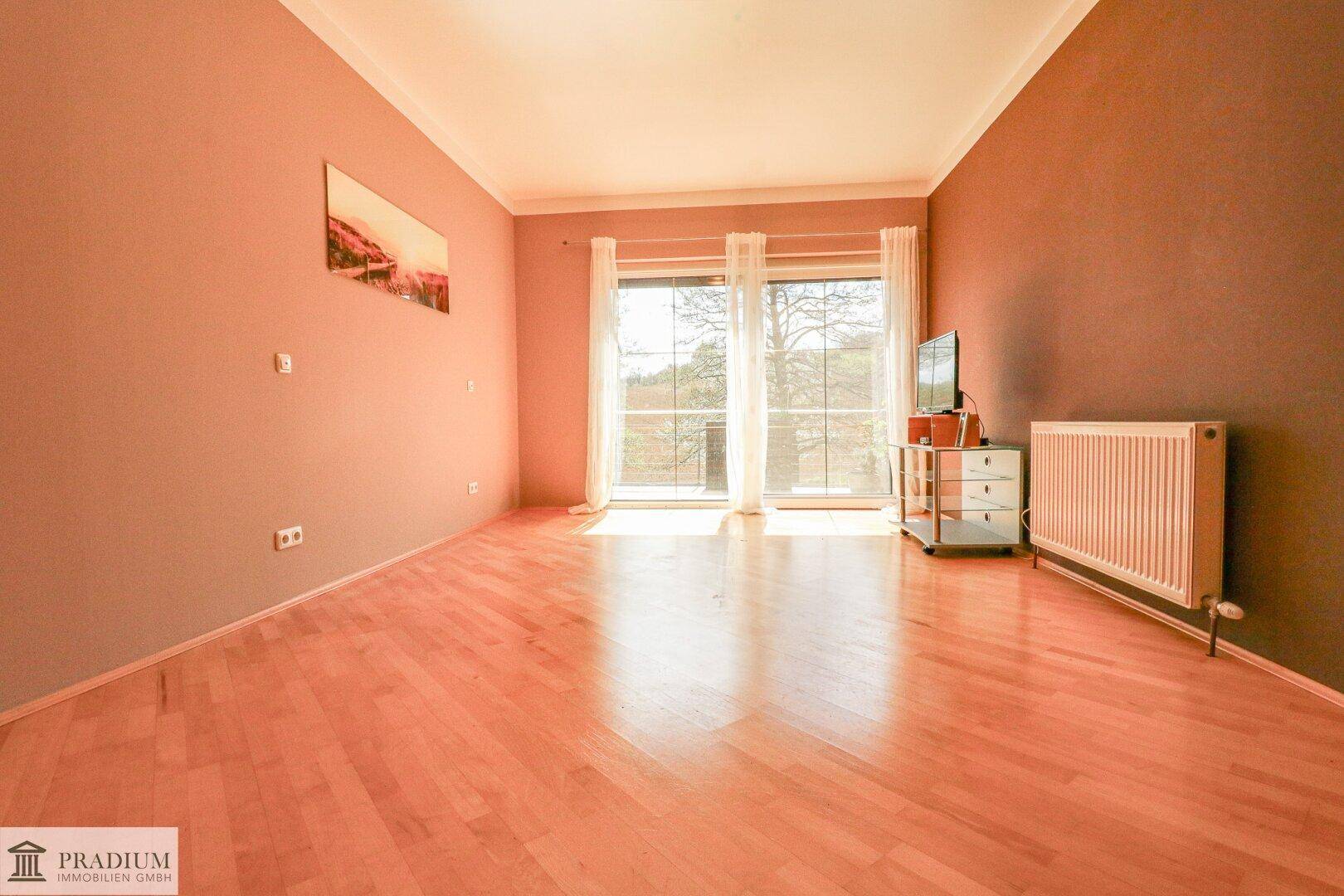 Wohnraum mit Parkettboden und großen Fenstern, die viel natürliches Licht hereinlassen.