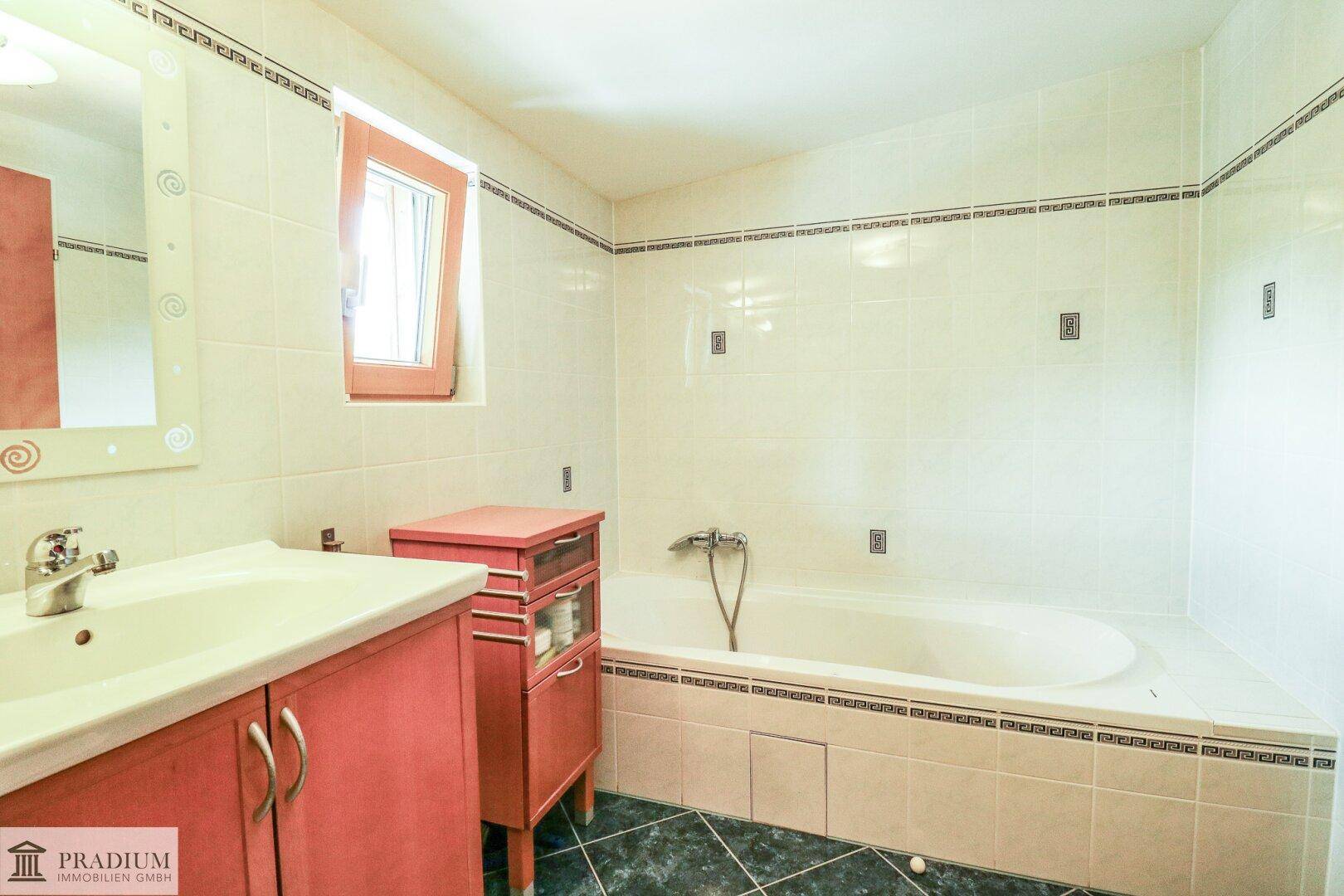 Badezimmer mit Badewanne, Waschtisch und Fenster, ausgestattet mit hellen Fliesen.