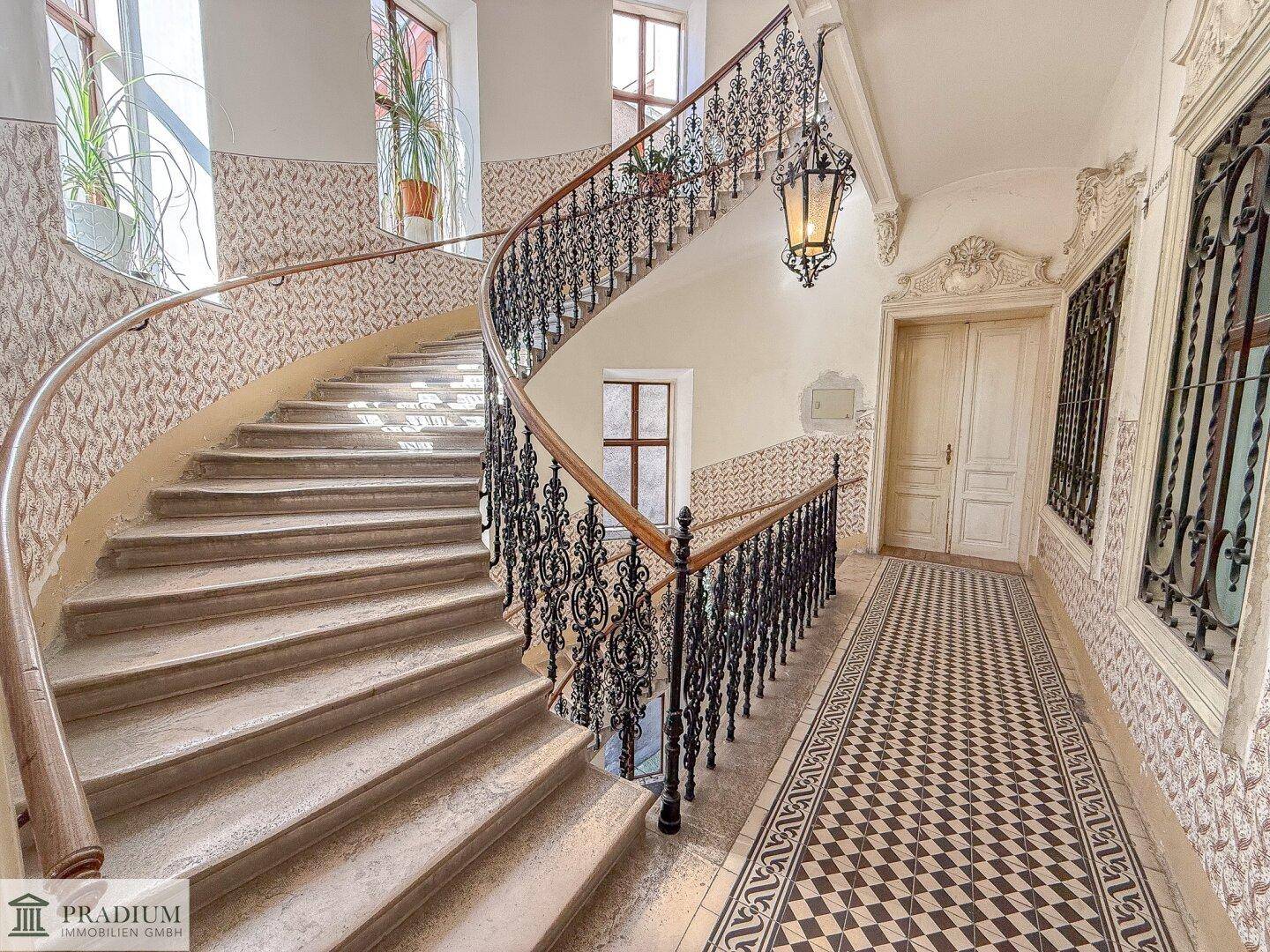 Elegantes Treppenhaus mit schmiedeeisernem Geländer, hohen Decken und historischen Fliesenboden.