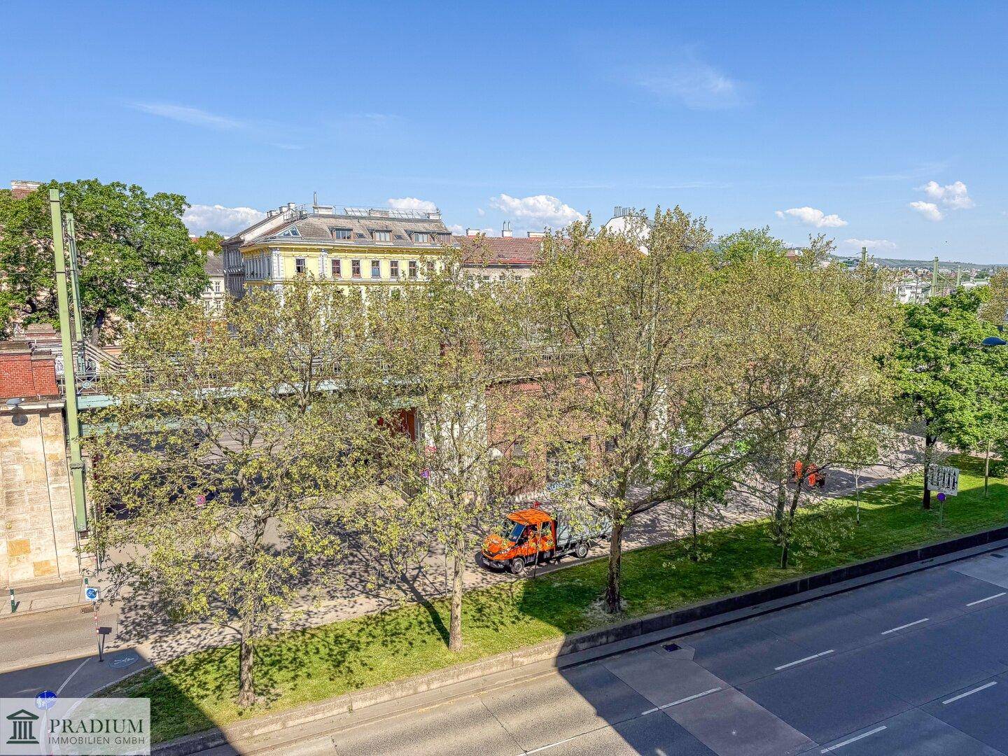 Blick über die Stadt mit Bäumen, einer Straße und umliegenden Gebäuden unter blauem Himmel.