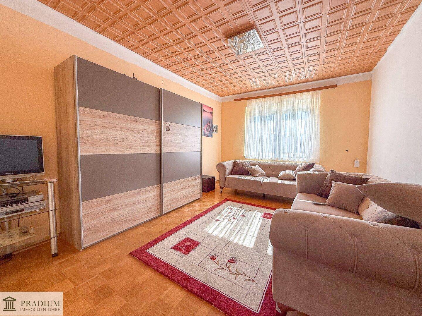 Gemütliches Wohnzimmer mit gemustertem Teppich, beigen Sofas und einer dekorativen Decke.