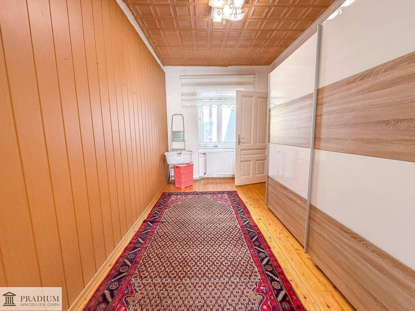 Schmaler Raum mit Holzpaneelen, einem großen Schiebetürenschrank und gemusterter Decke.