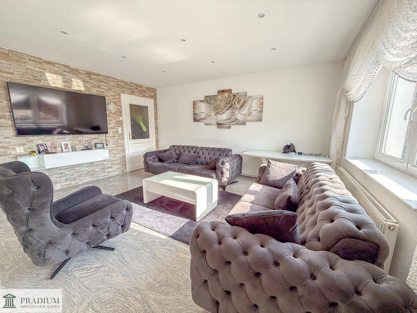 Helles Wohnzimmer mit Steinwandakzent, modernen Sofas und einem großen Fernseher an der Wand.