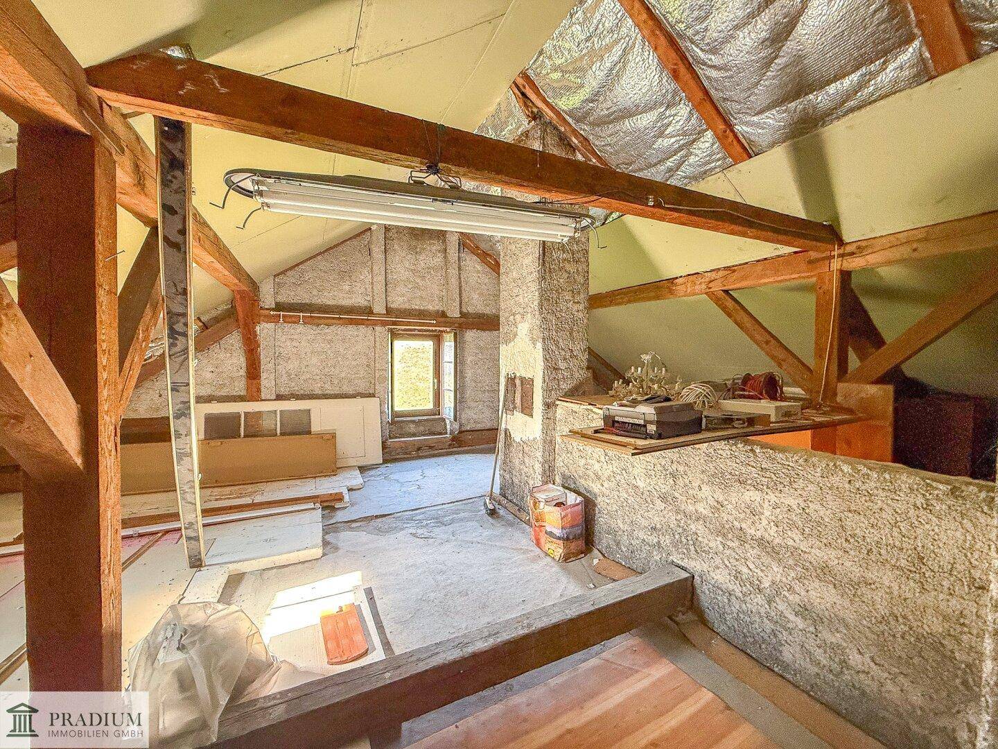 Unfertiger Dachboden mit sichtbaren Holzbalken und Isolierung, bereit für den Ausbau.