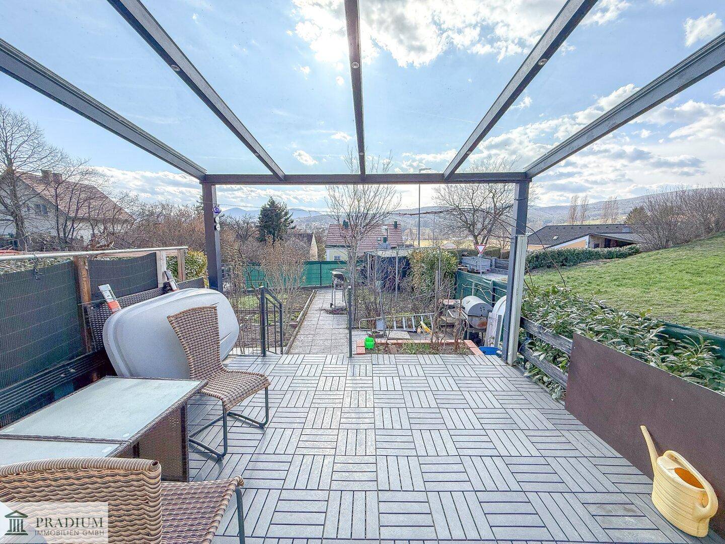 Überdachte Terrasse mit Fliesenboden, Gartenmöbeln und einem weiten Blick ins Grüne.