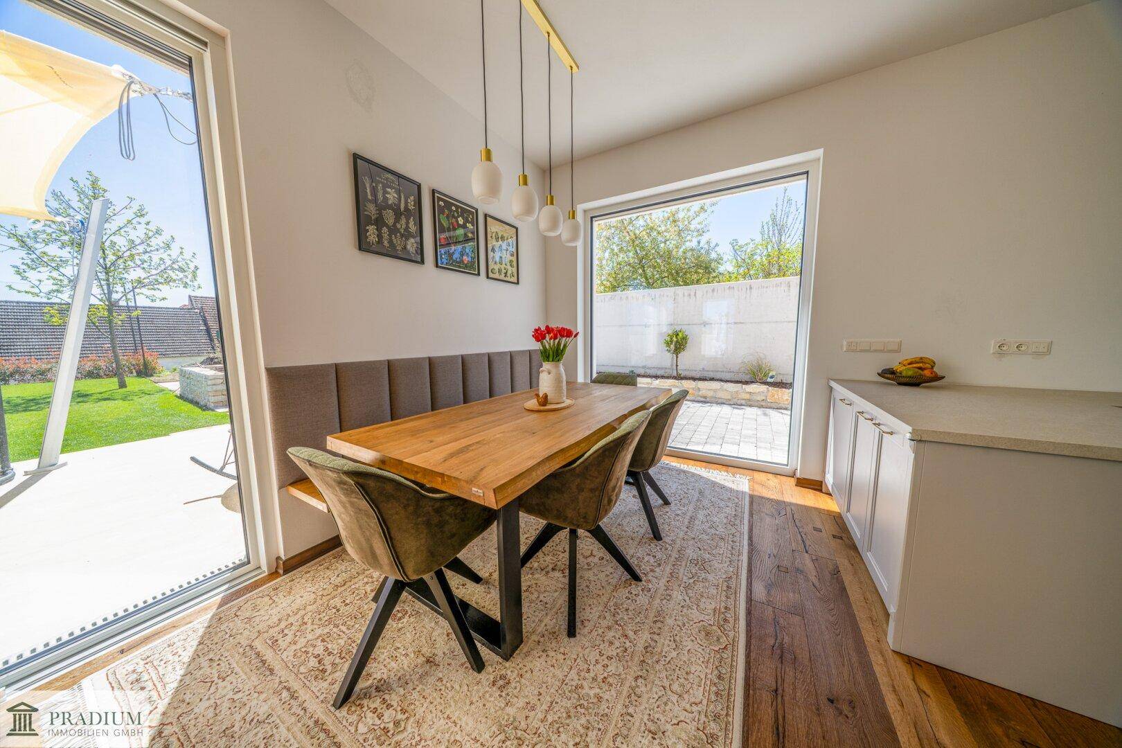 Heller Essbereich mit Holztisch, Sitzbank und großen Fenstern zum Garten.