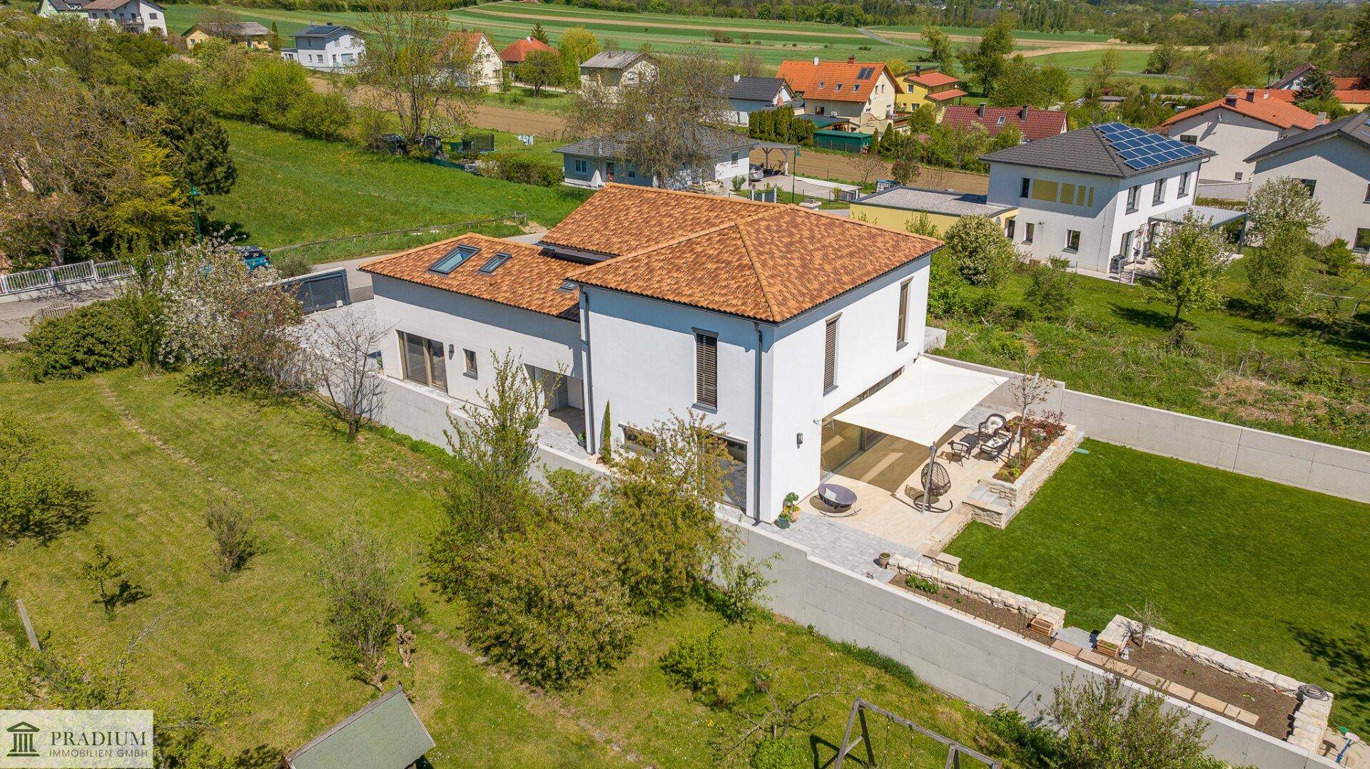 Luftaufnahme eines modernen Hauses mit Ziegeldach und weitläufigem Grundstück in grüner Umgebung.
