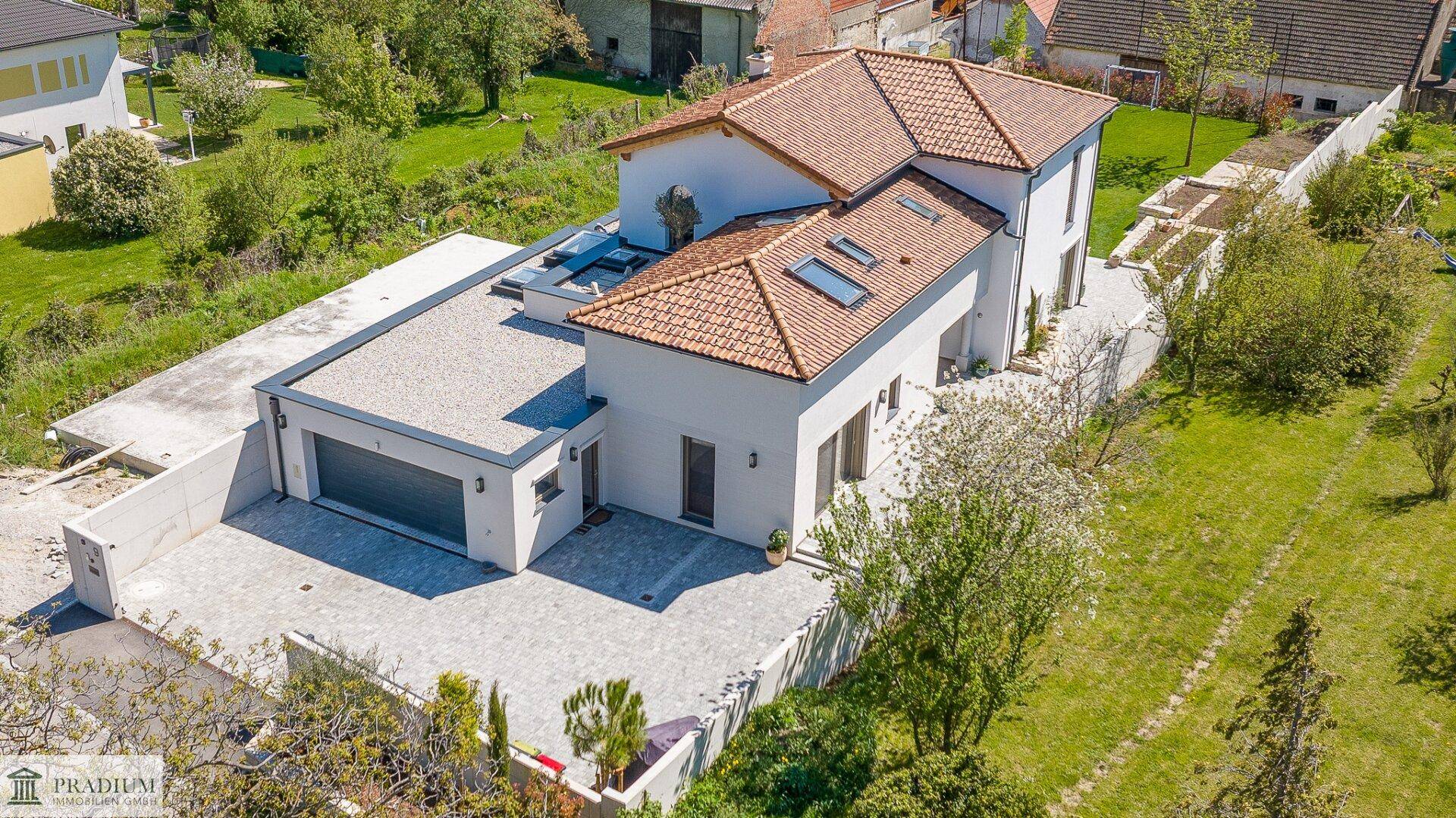 Vogelperspektive eines modernen Wohnhauses mit Garage, gepflasterter Zufahrt und Gartenbereich.